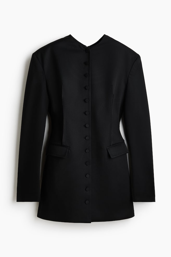 Um vestido blazer preto apresenta um decote redondo, mangas compridas e uma longa fileira de botões pretos ao longo da parte frontal central, com dois bolsos de aba a detalhar as ancas. - 1