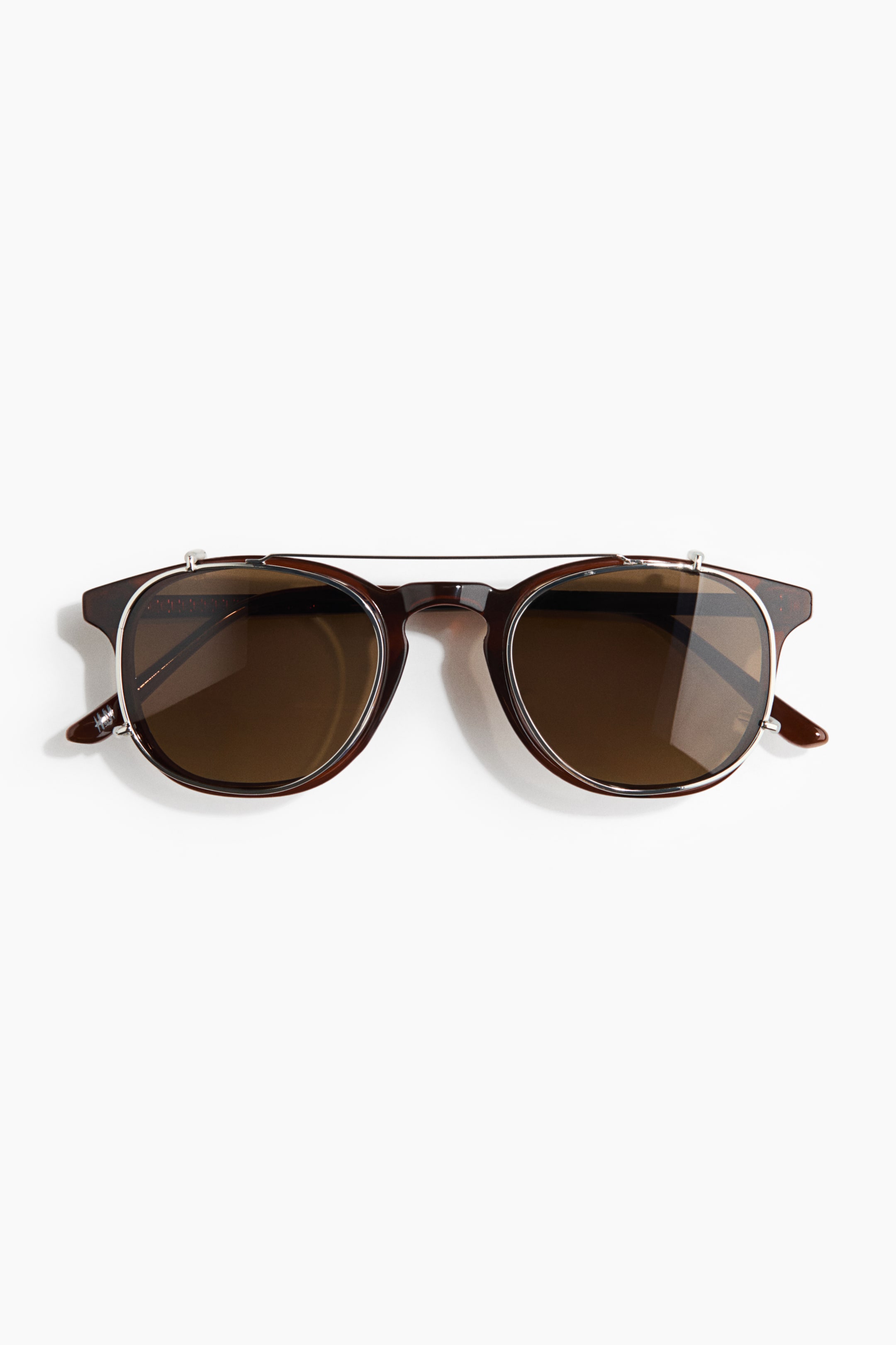View larger image: These sunglasses showcase brown tortoiseshell frames paired with round brown lenses. A silver-toned metal clip-on frame elegantly sits over the main frame, creating a stylish double bridge.