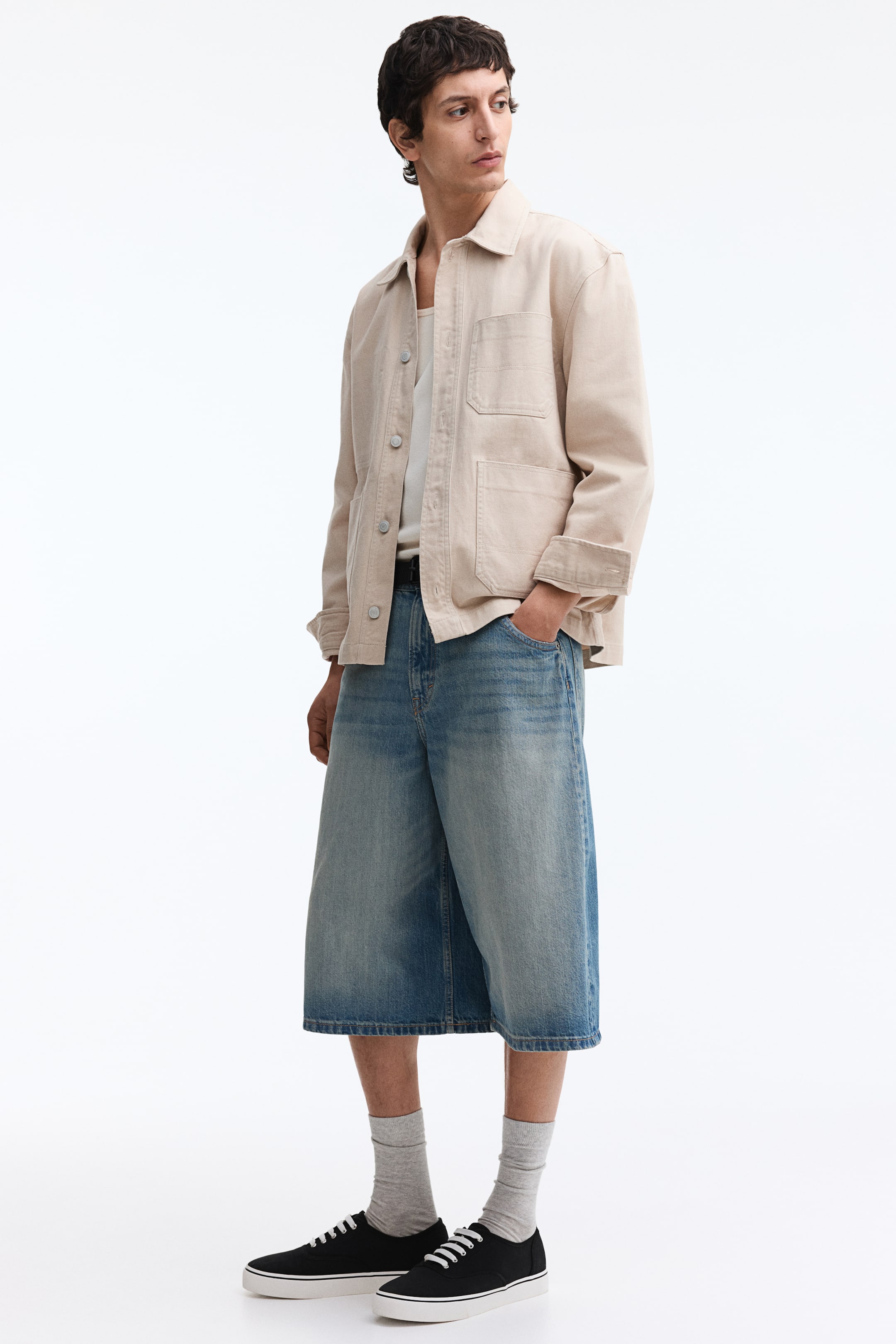 View larger image: A light beige utility jacket is styled open over a white tank top, featuring a spread collar, four front patch pockets, and long sleeves casually rolled up at the cuffs. The jacket showcases a relaxed fit.