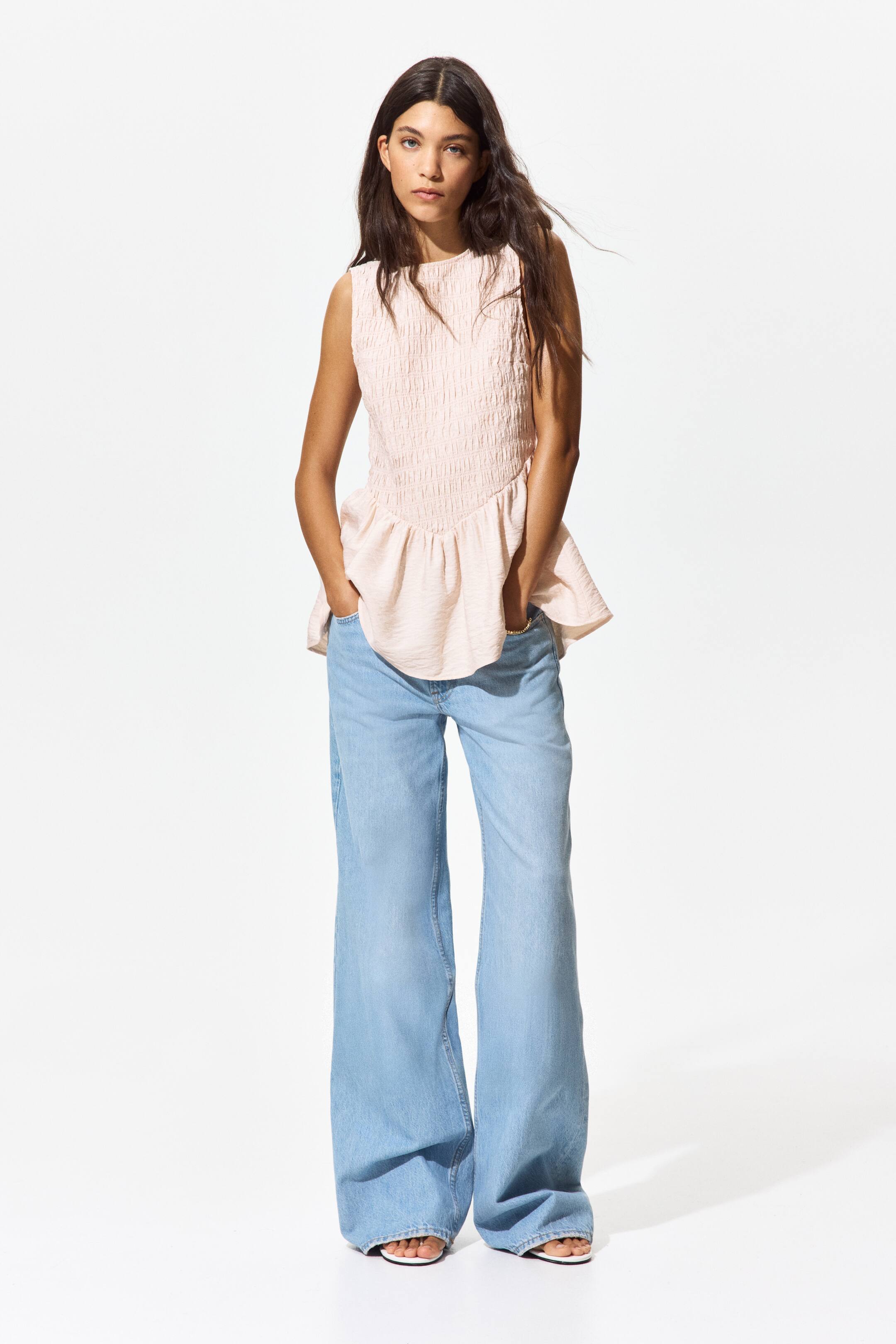 View larger image: This light pink sleeveless peplum top is showcased at the front. It features a smocked bodice with a round neckline, and a gathered peplum hem that flares out from the waist.