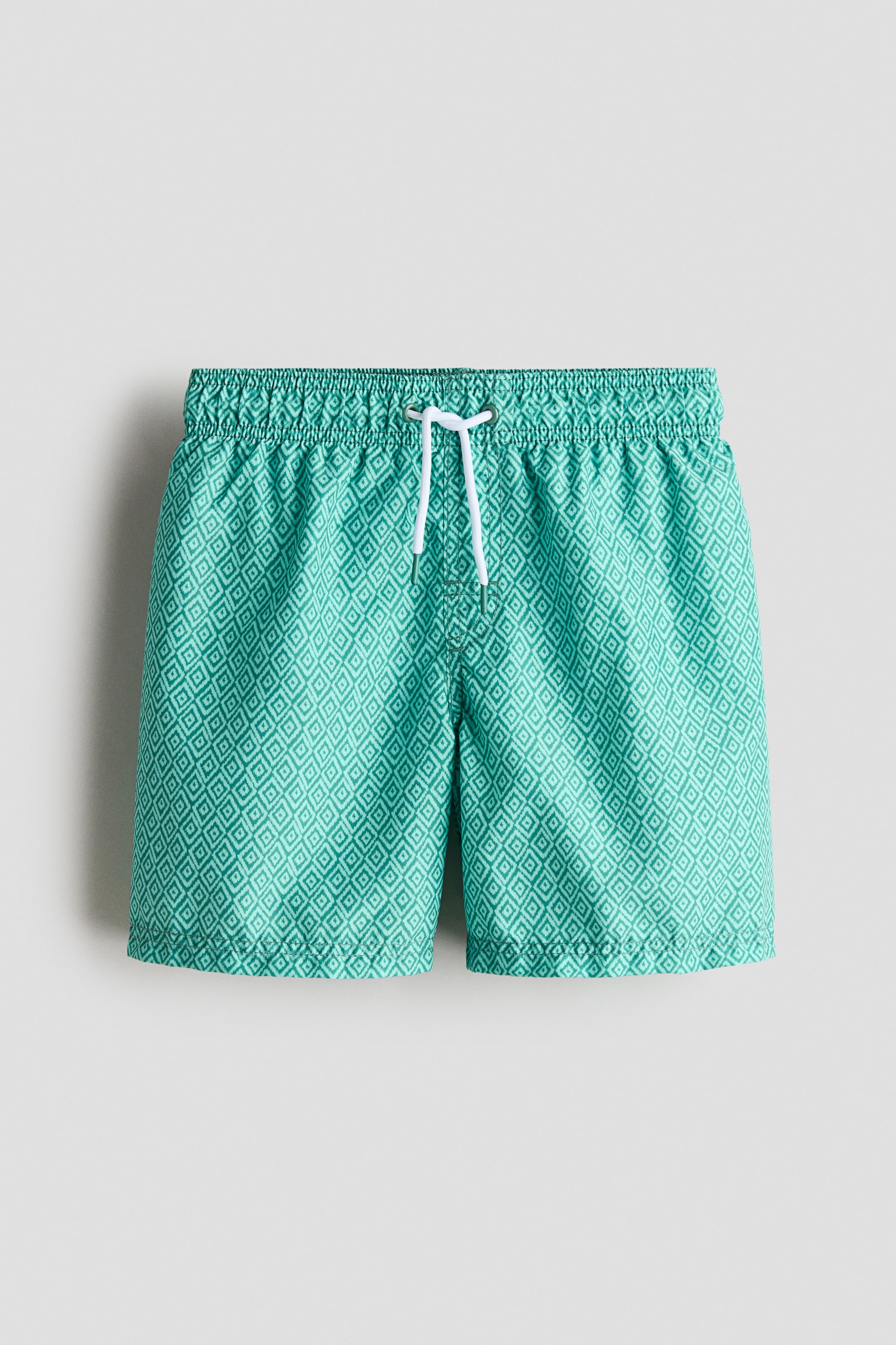 Ver imagen más grande: Los pantalones cortos de baño muestran un color aguamarina con un patrón repetido de diamantes en verde claro. Presentan una cintura elástica con un cordón blanco que se ata en la parte delantera.