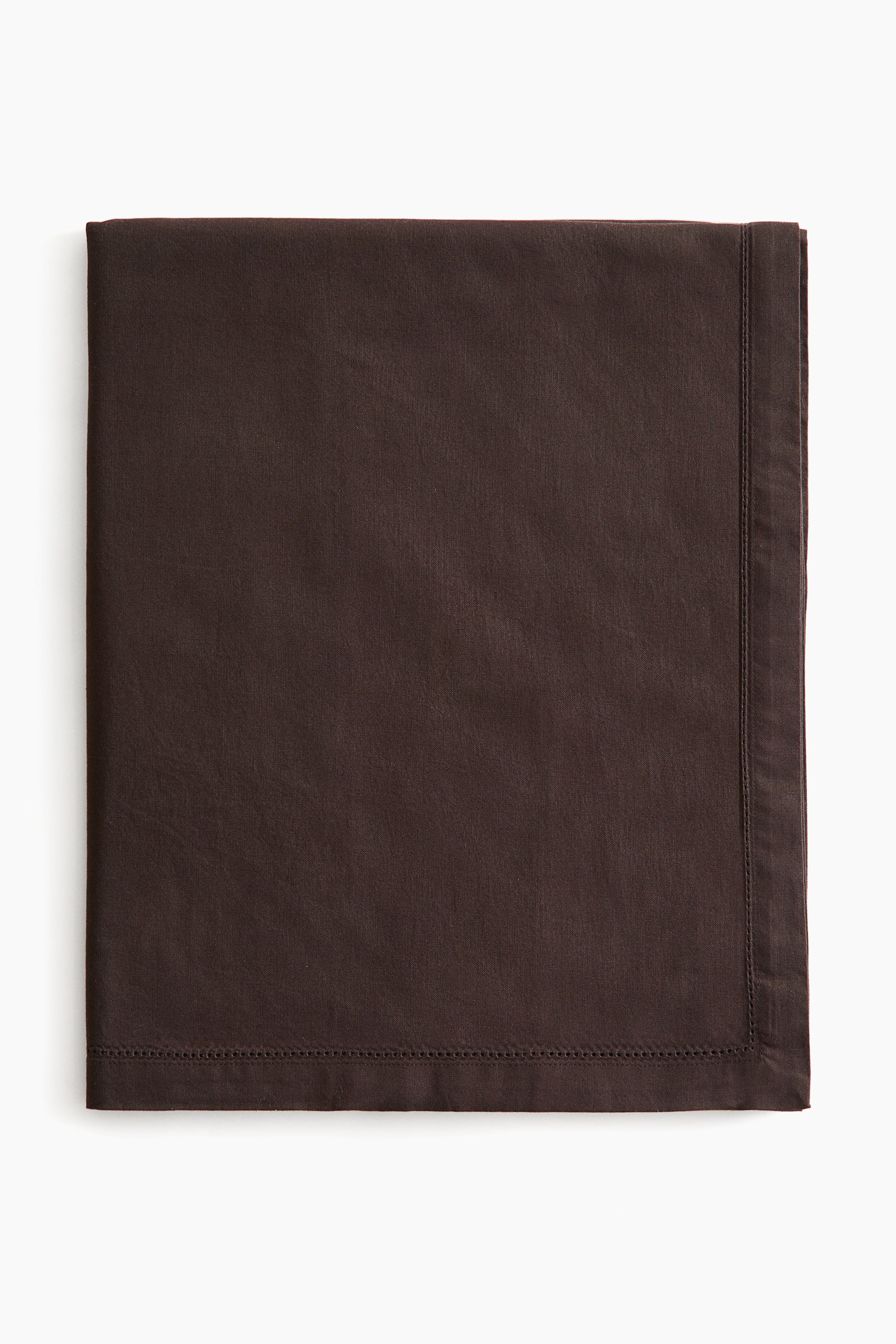 View larger image: A dark brown cotton canvas tablecloth is resting folded in a front-facing view, displaying its smooth matte texture. The fabric features a wide hem with decorative hemstitch detailing running along the inner edges.