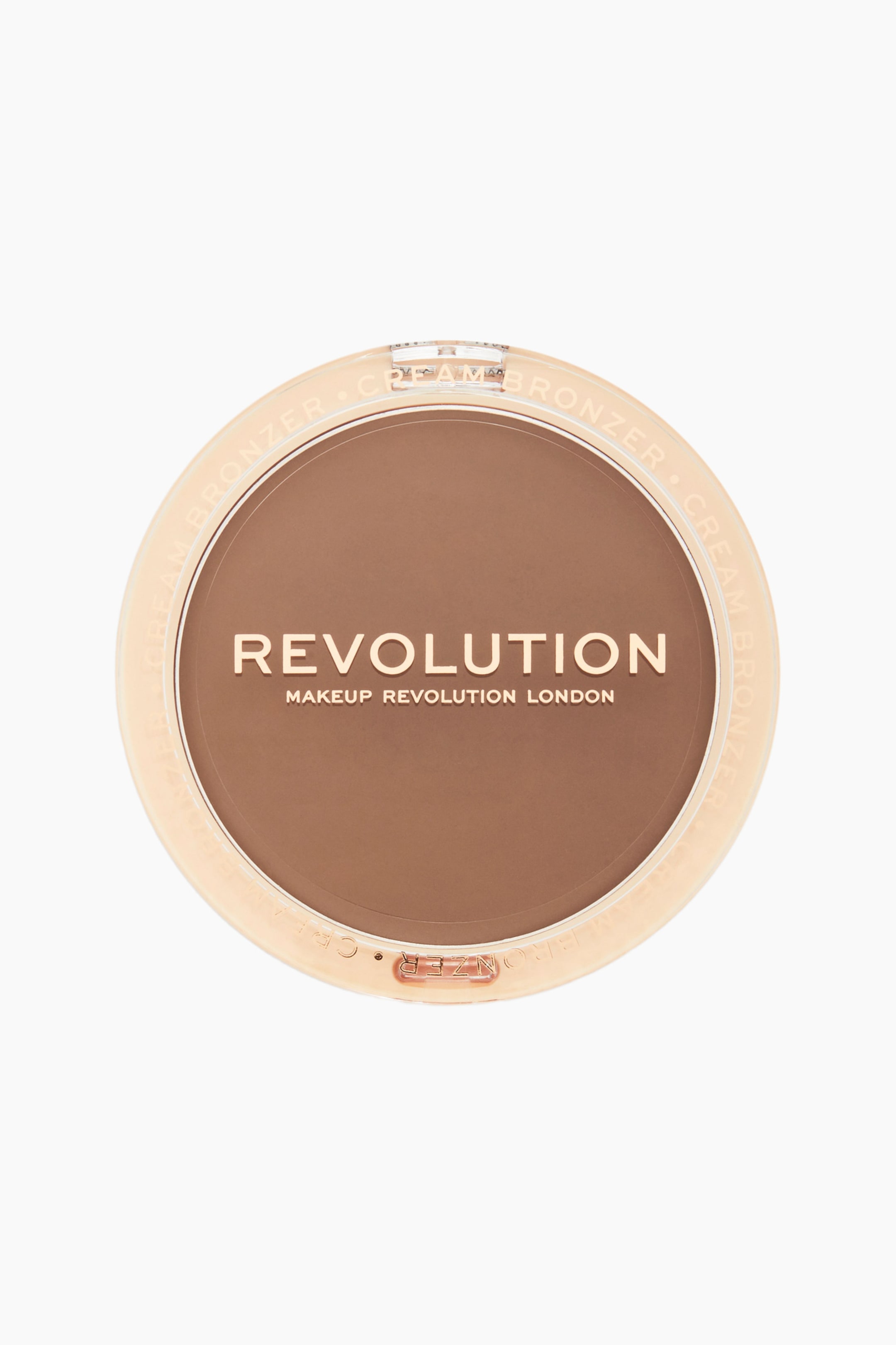 Visa större bild: En rund bronzerkompakt i kräm ligger platt i en uppifrånvy och har ett klart, ljuspersikofärgat plastlock som avslöjar en len, matt brun krämprodukt. Locket visar logotypen "REVOLUTION MAKEUP REVOLUTION LONDON" i guldfärgad text över mitten, med "CREAM BRONZER" präglat längs den cirkelformade kanten.