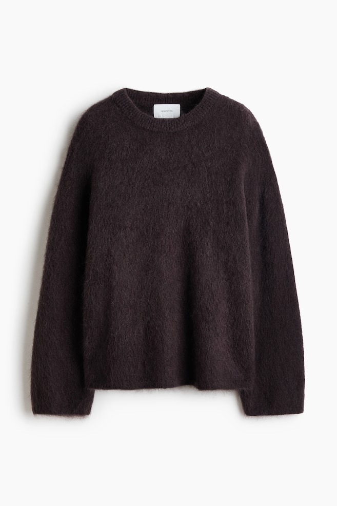 An oversized, dark brown knitted jumper is shown from the front, showcasing its fuzzy, soft-knit texture containing mohair and wool. The jumper features dropped shoulders, long sleeves, a ribbed crew neck, and subtle ribbing at the cuffs and hem. - 1