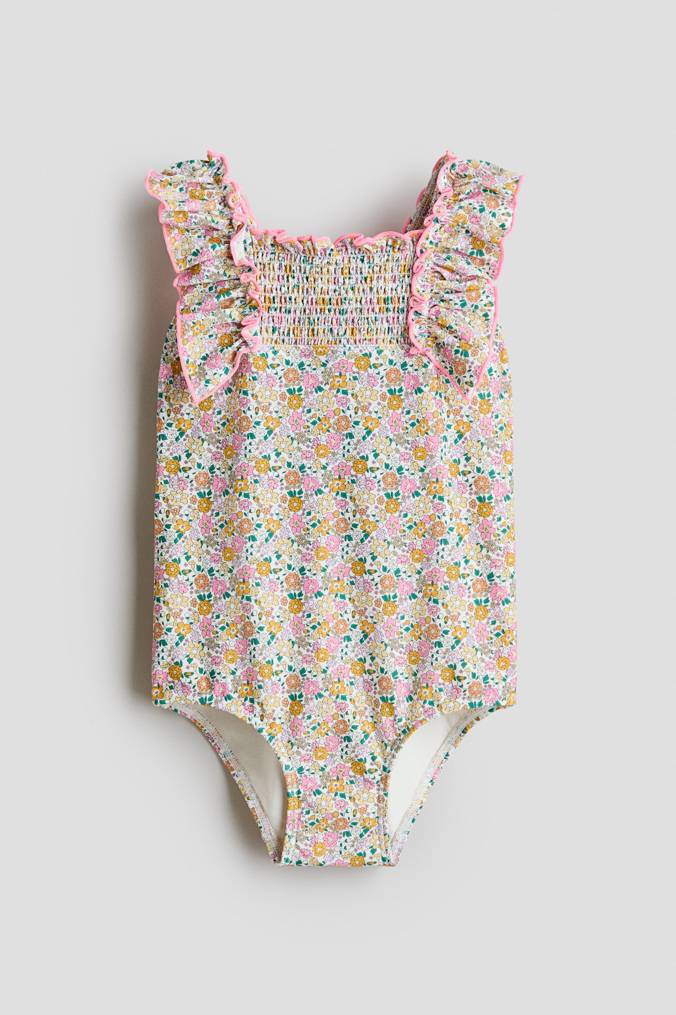View larger image: A front-facing fully lined swimsuit showcases an all-over floral print in pink, yellow, and green. It features a square neckline, a smocked section across the front, and frill-trimmed shoulder straps with pink trim.