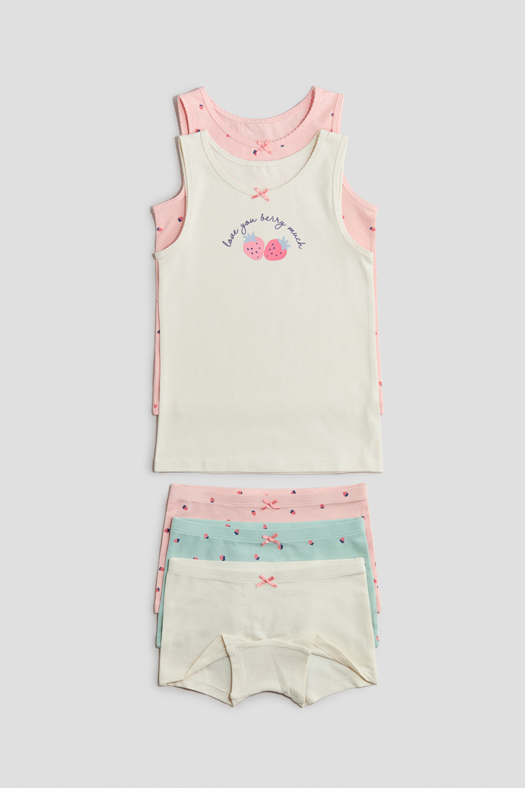 查看大圖: 這是一組包含兩件背心和三條配套內褲的套裝。前面的米白色背心上印有“love you berry much”草莓圖案，層疊在一件粉色圖案背心上，兩件背心的領口和袖口均有小波浪邊裝飾。下方疊放著三條內褲，每條內褲的腰部都配有一個小粉色蝴蝶結，顏色分別為淺粉色、薄荷綠和米白色，其中粉色和薄荷綠的內褲上有細緻的莓果圖案。