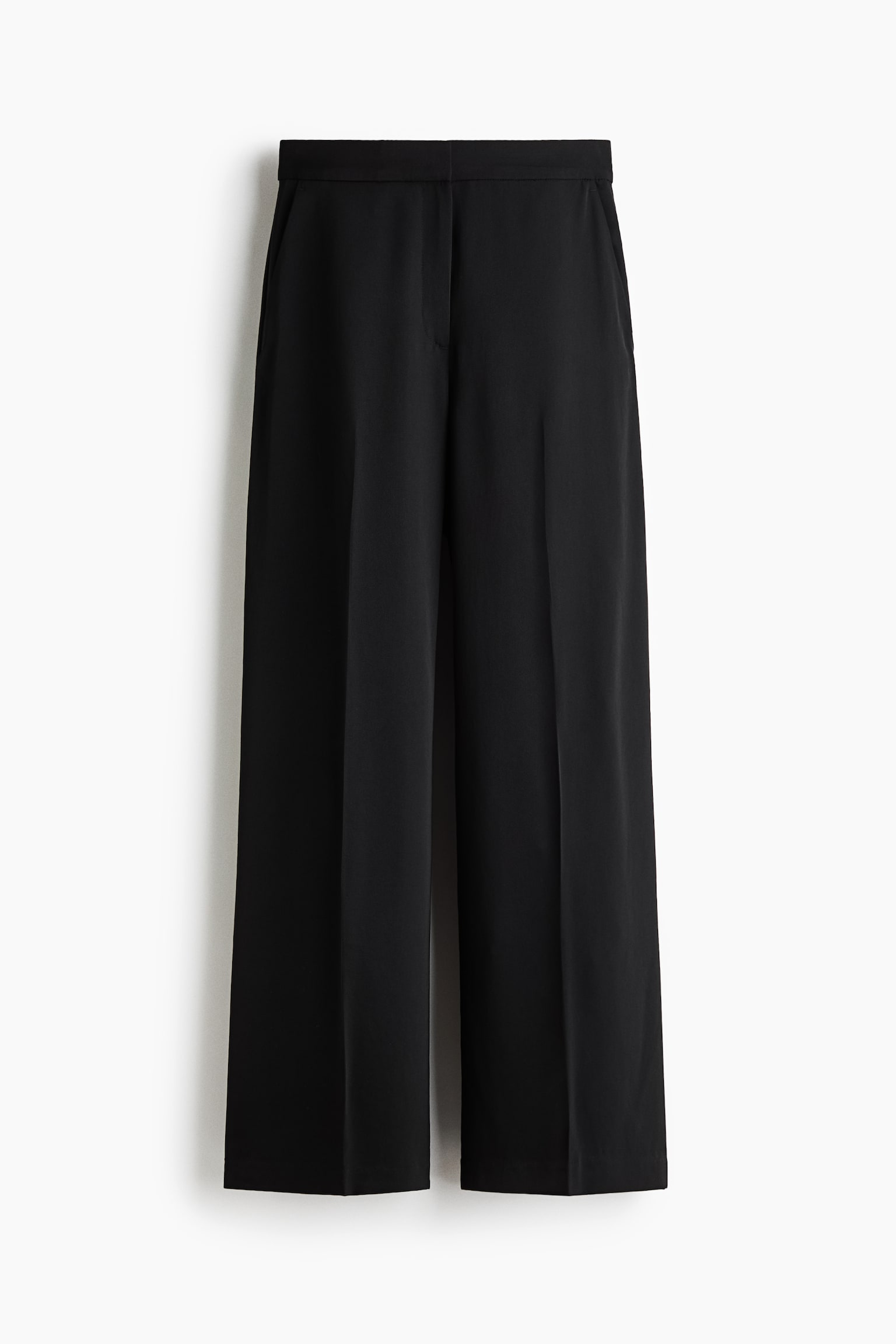 A pair of black wide-leg trousers is shown from the front, featuring a clean, structured waistband with a concealed fastening. The trousers drape into a wide-leg silhouette with sharp pressed creases running down the centre of each leg.