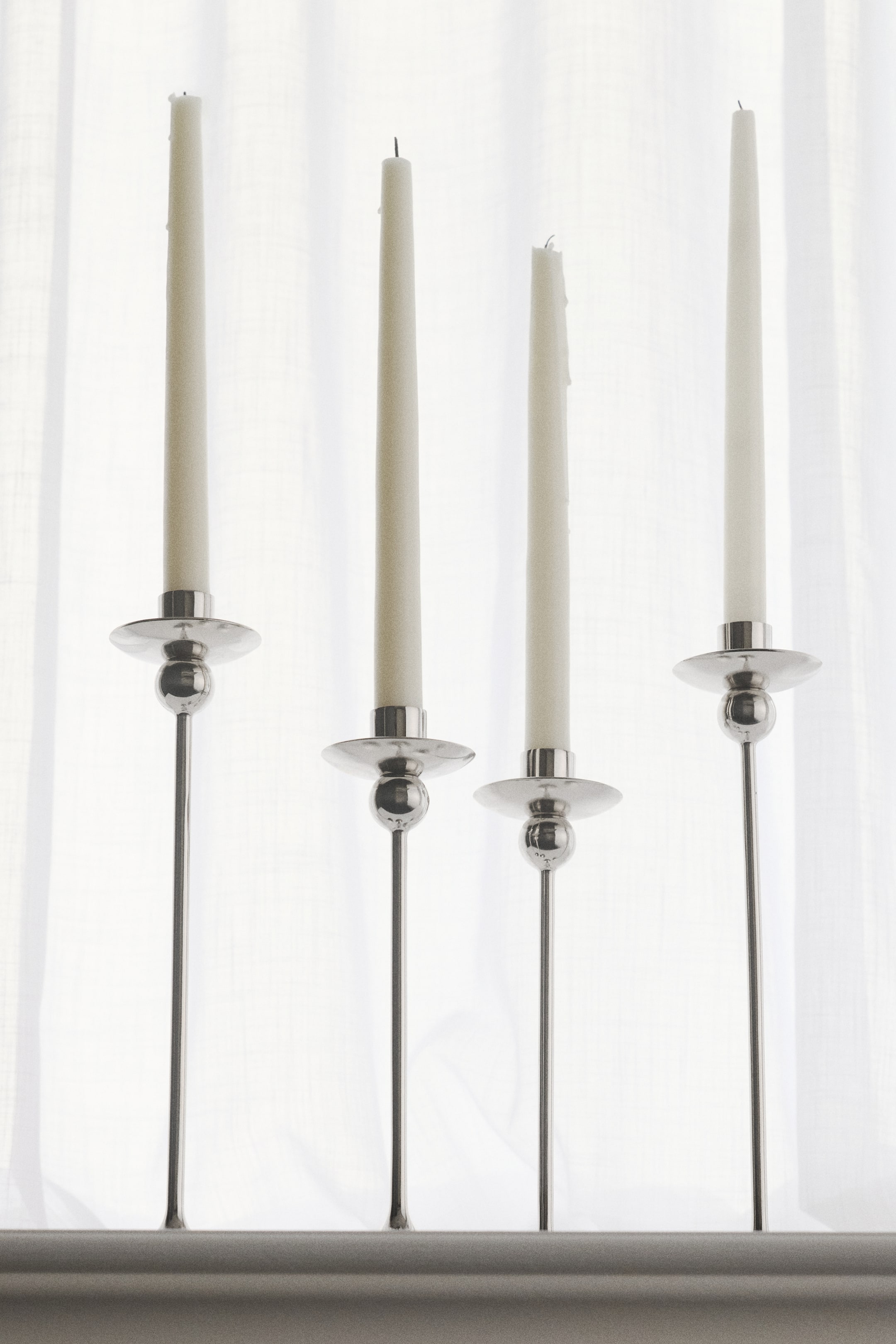 View larger image: A tall candlestick in polished stainless steel features a sleek design, showcasing a spherical detail on its stem and holding a white taper candle.