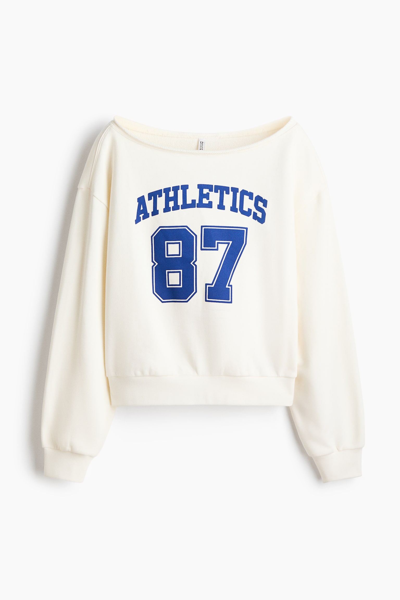 A front-facing cream-colored sweatshirt is featuring a wide boatneck, dropped shoulders, and long sleeves with ribbed cuffs. The chest is displaying a blue varsity-style graphic with the arched text "ATHLETICS" above the number "87".