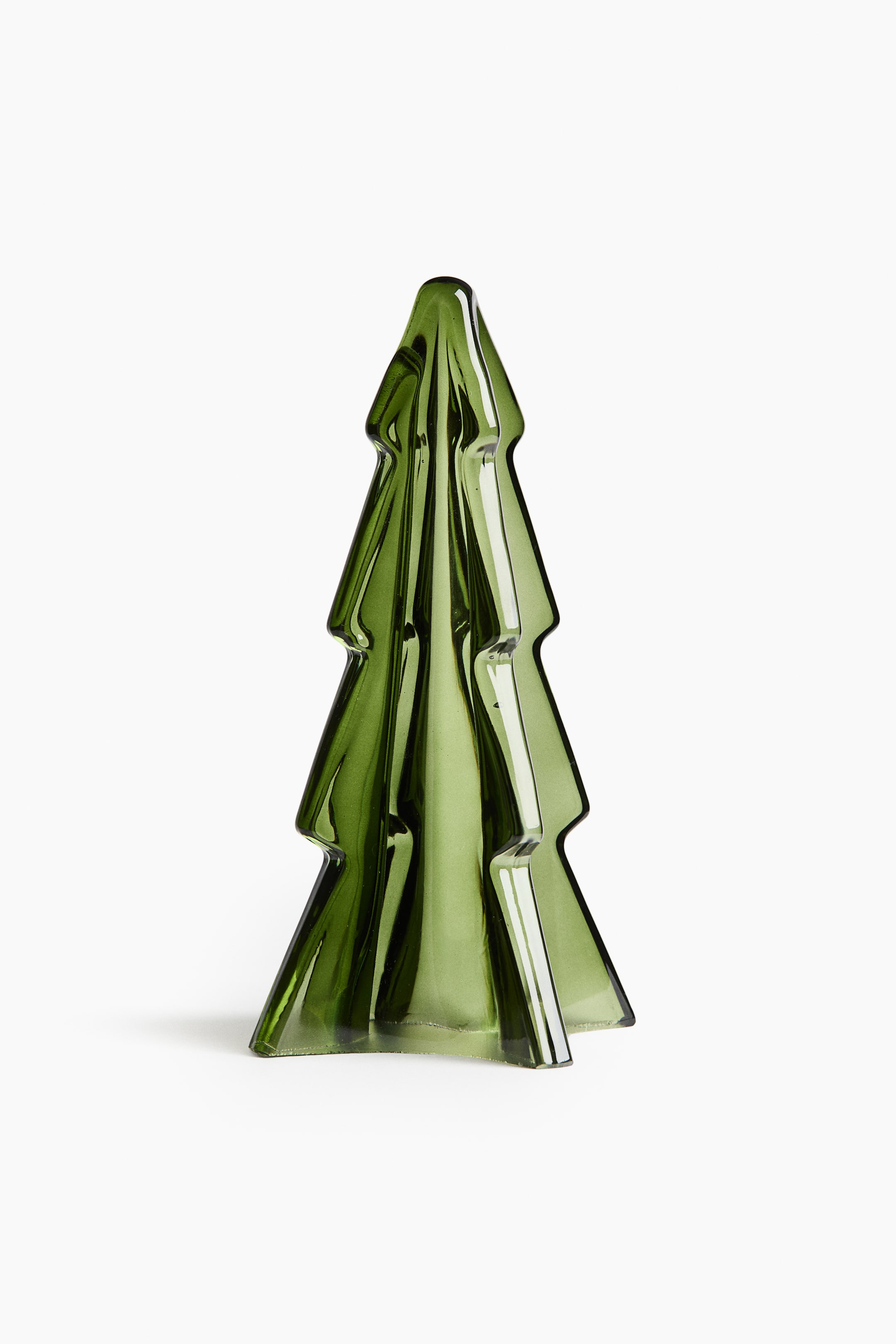 Ampliar la imagen: Una decoración navideña de vidrio con forma de árbol de pino está de pie, de frente, mostrando su color verde translúcido y una estructura estilizada de tres niveles. La decoración presenta profundas estrías verticales que se estrechan hacia una punta redondeada, creando una apariencia texturizada y tridimensional.