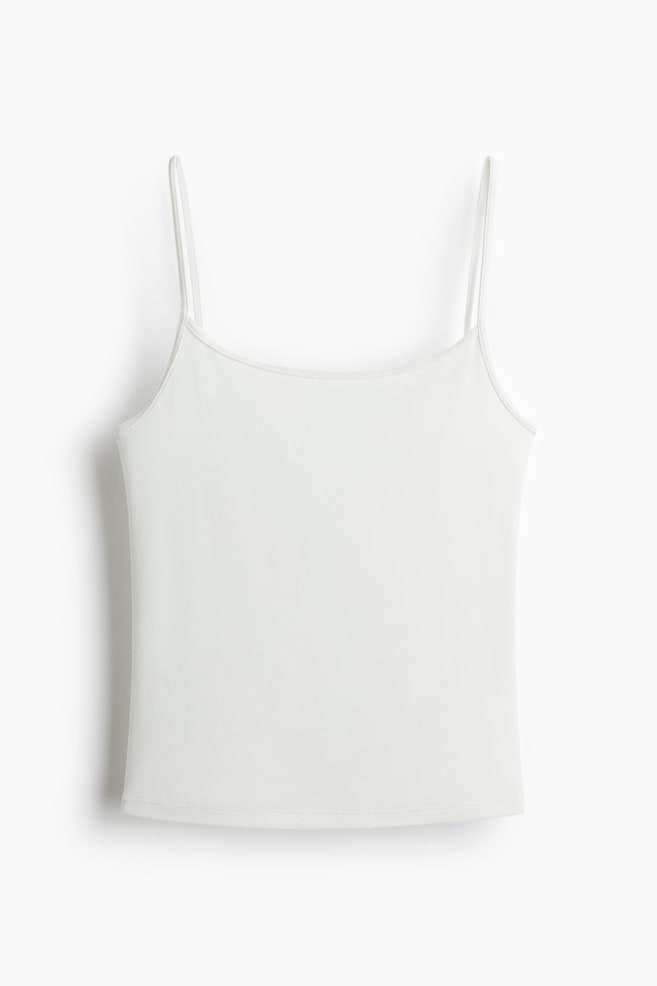 A white camisole top shown from the front, featuring thin spaghetti straps, a scoop neckline and a straight hem. - 1