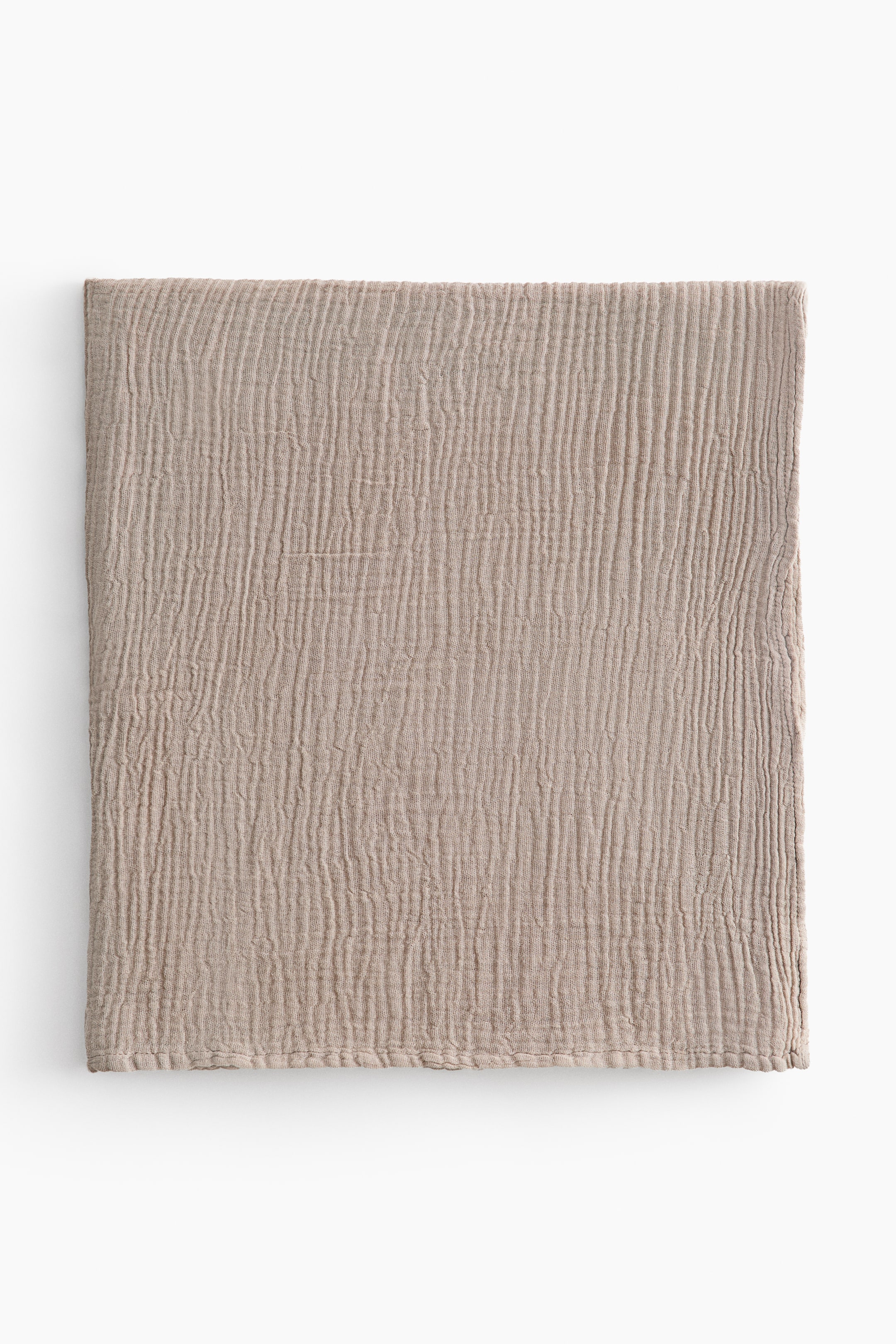 View larger image: A cotton muslin baby blanket is shown folded into a square, displaying a highly textured, crinkled surface in a light taupe color. The blanket features vertical puckered lines and a subtly stitched bottom edge.