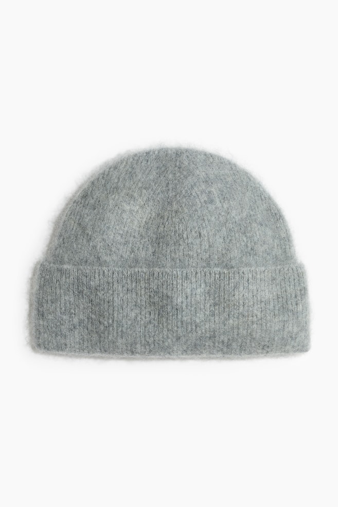 Un bonnet en maille gris prÃ©sente une texture douce et duveteuse, avec un large revers repliÃ© cÃ´telÃ© et une calotte arrondie, vu de face. - 1