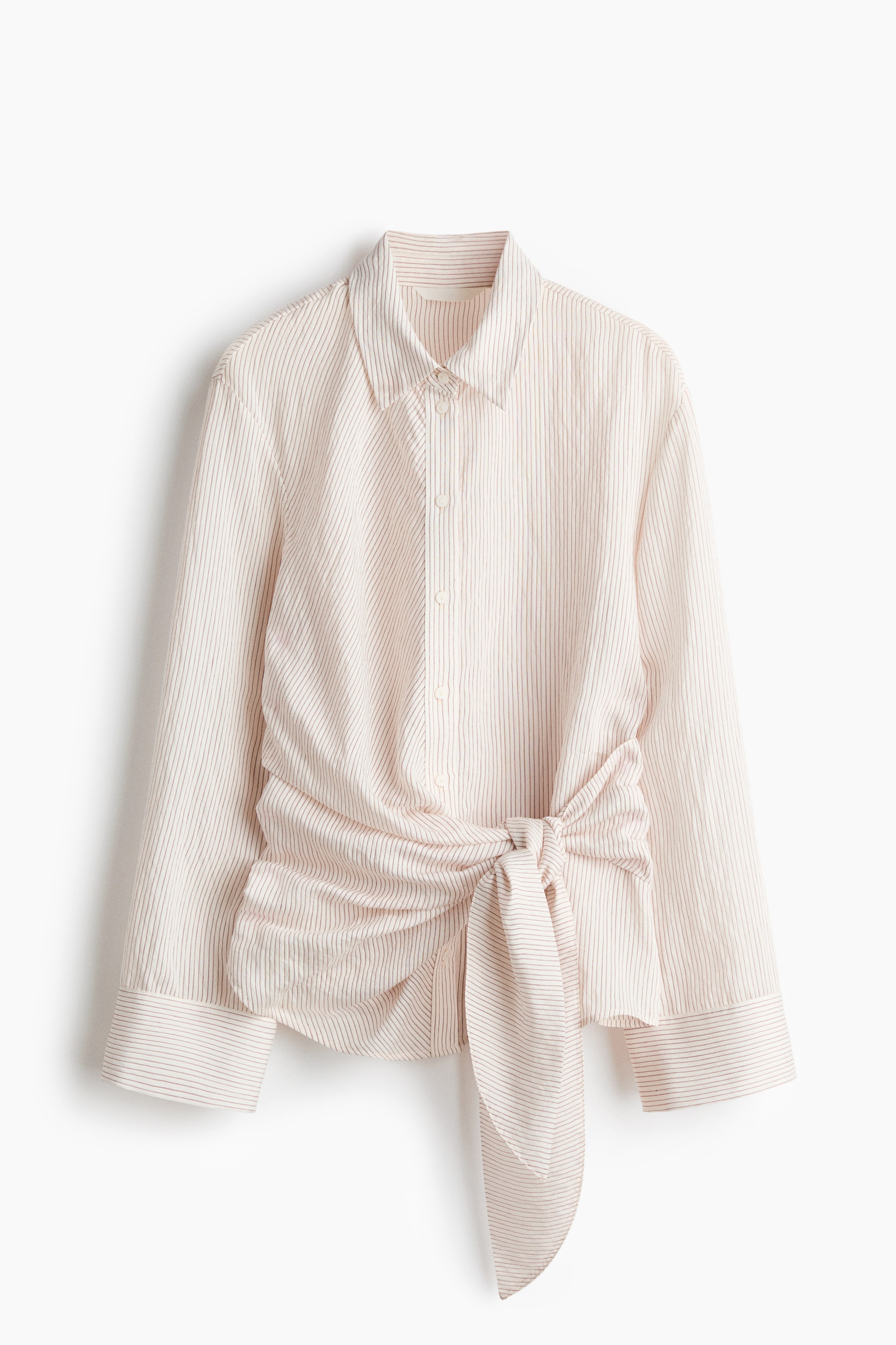 Grotere afbeelding bekijken: Een lichte, verticaal gestreepte blouse in een viscose-mix weefsel toont zijn voorkant, met een kraag, knopen aan de voorkant en lange mouwen met knoopsluitingen. Brede linten worden aan de voorkant van de taille geknoopt, wat zorgt voor plooien.