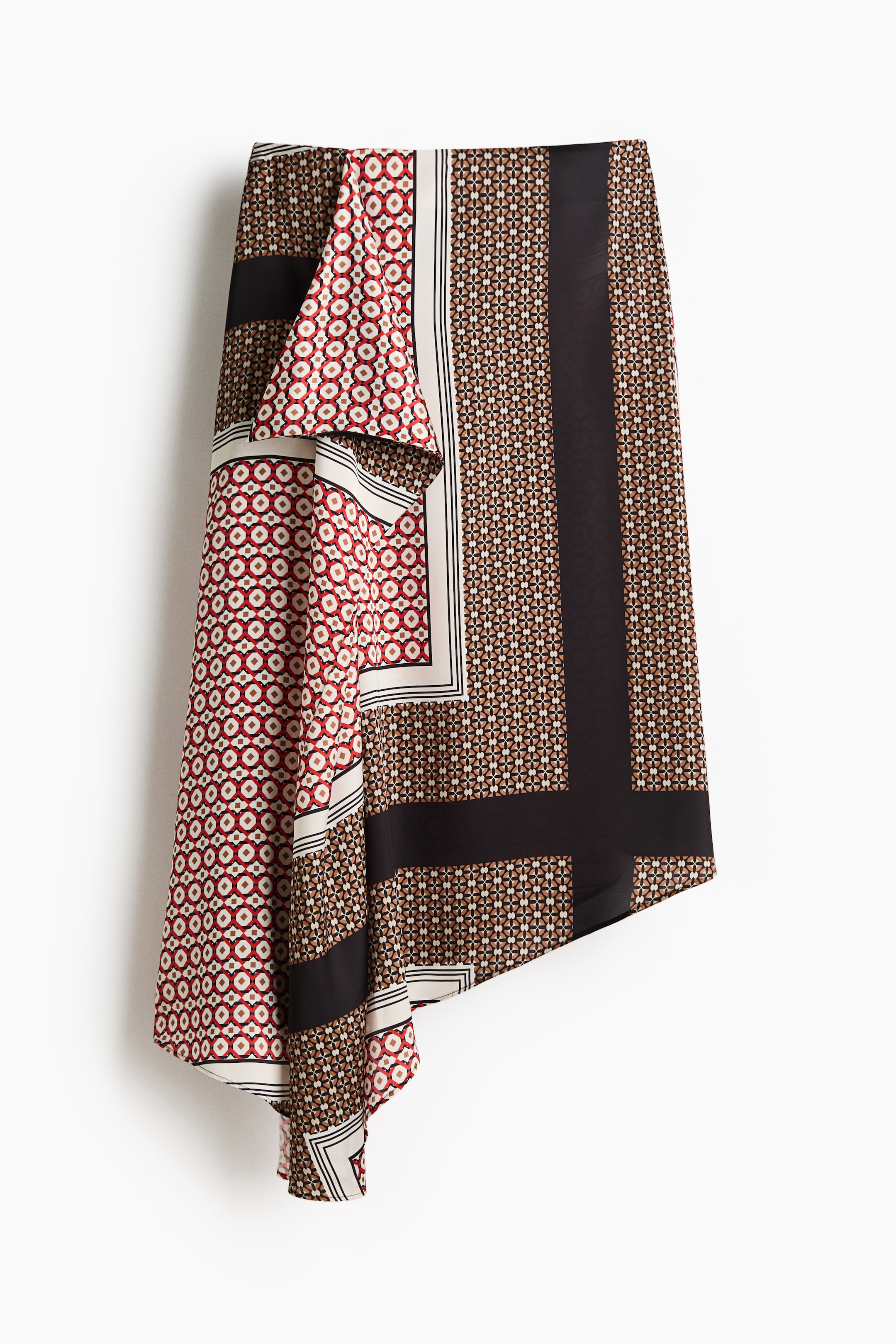 Grotere afbeelding bekijken: De VOORKANT van een asymmetrische rok toont een patchwork van geometrische patronen in rood, wit, zwart en bruin. Het heeft onderscheidende panelen met kleine cirkelvormige patronen en zich herhalende vormen, gescheiden door stevige zwarte banden en zwart-wit gestreepte randen, wat een geplooide, ongelijke zoomlijn creëert.