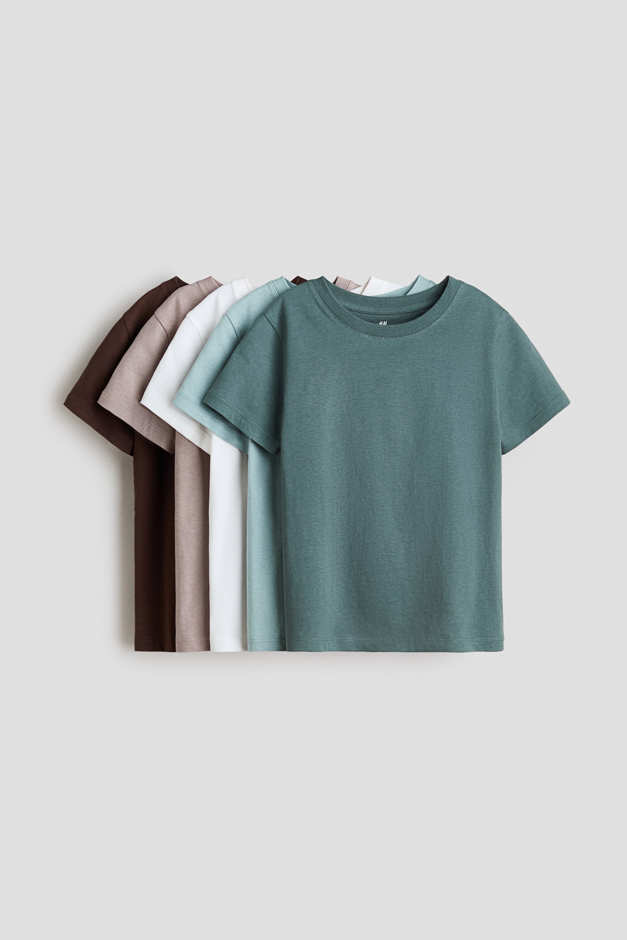 View larger image: Soft cotton jersey T-shirts feature a round neckline and a straight-cut hem. Multiple shirts in shades of green, light blue, white, light brown, and dark brown are overlapping, all facing forward.