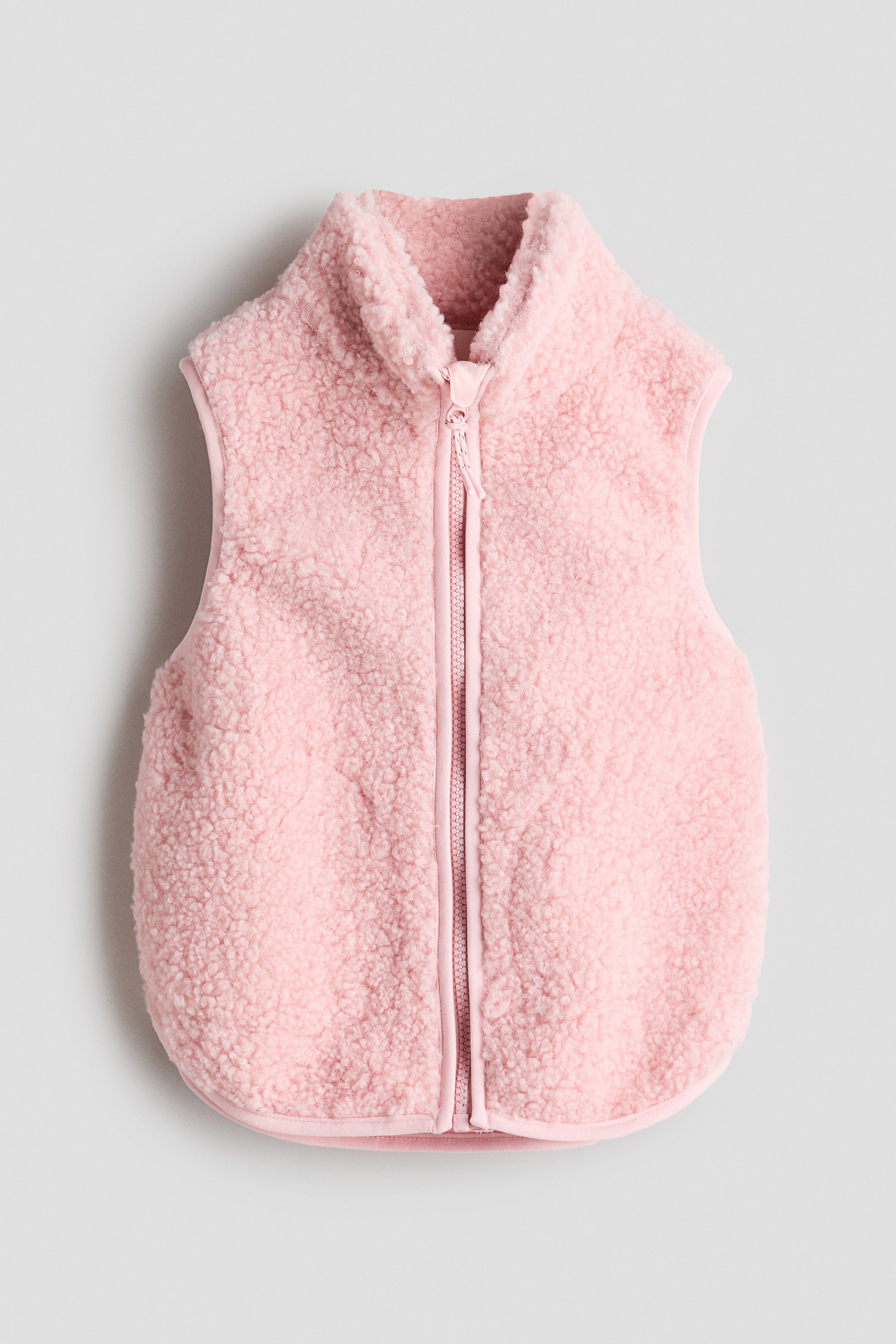 View larger image: A pink sherpa vest is showcased from the front, highlighting its plush texture and full-zip fastening. It features a stand-up collar and a rounded bottom hem.