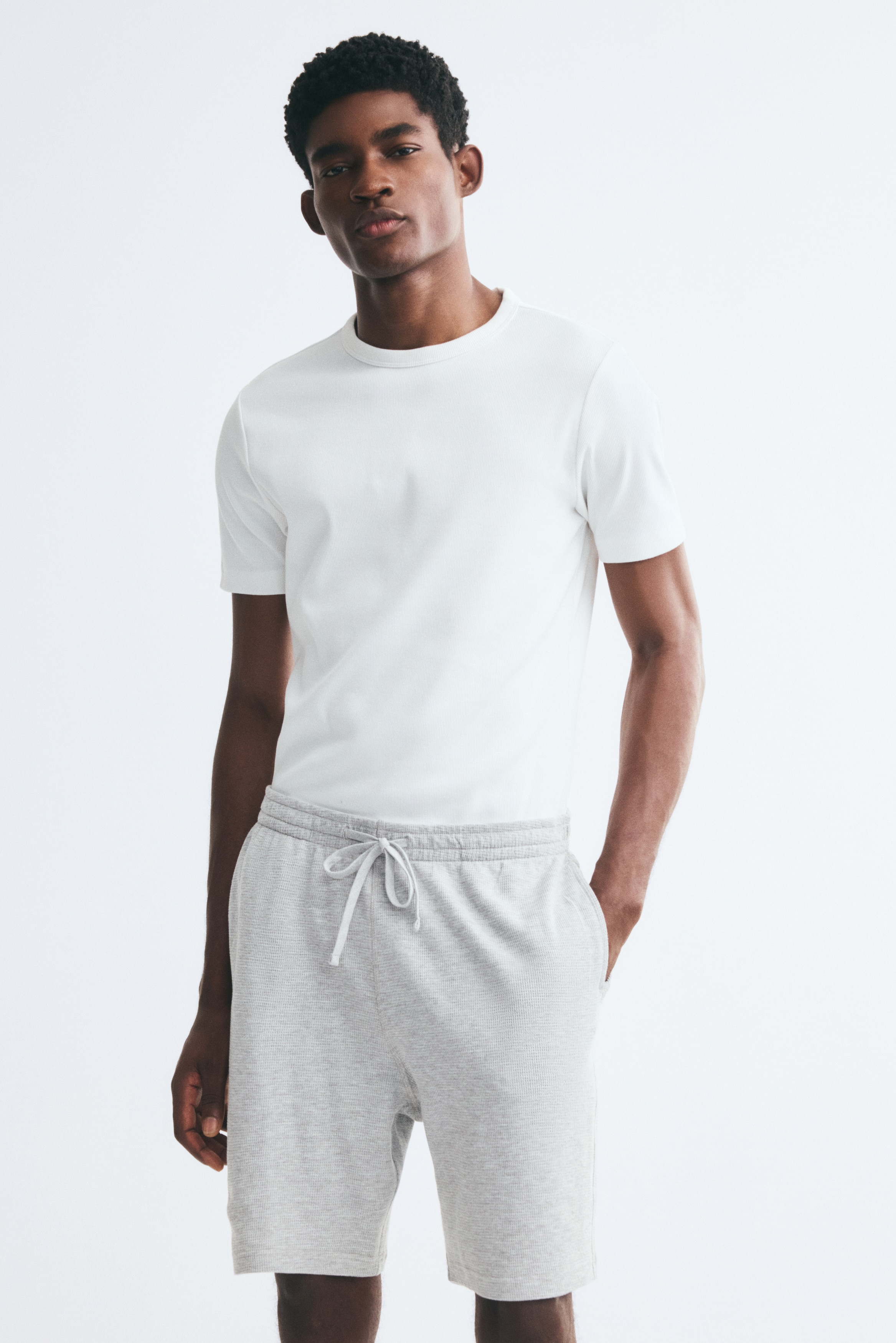 Front-facing grey waffle knit shorts come with an elasticated waistband and a white drawstring. The side pockets are visible.