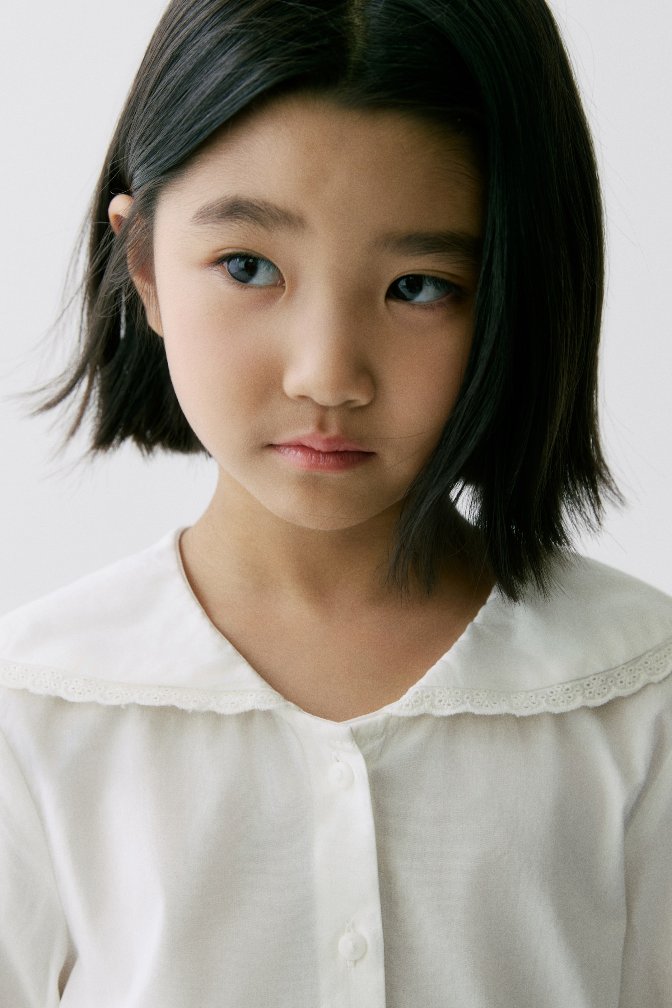 查看大圖: 白色女襯衫由正面展示，配有圓領並以精緻蕾絲飾邊，前襟為排扣設計，可見兩顆白色鈕扣。