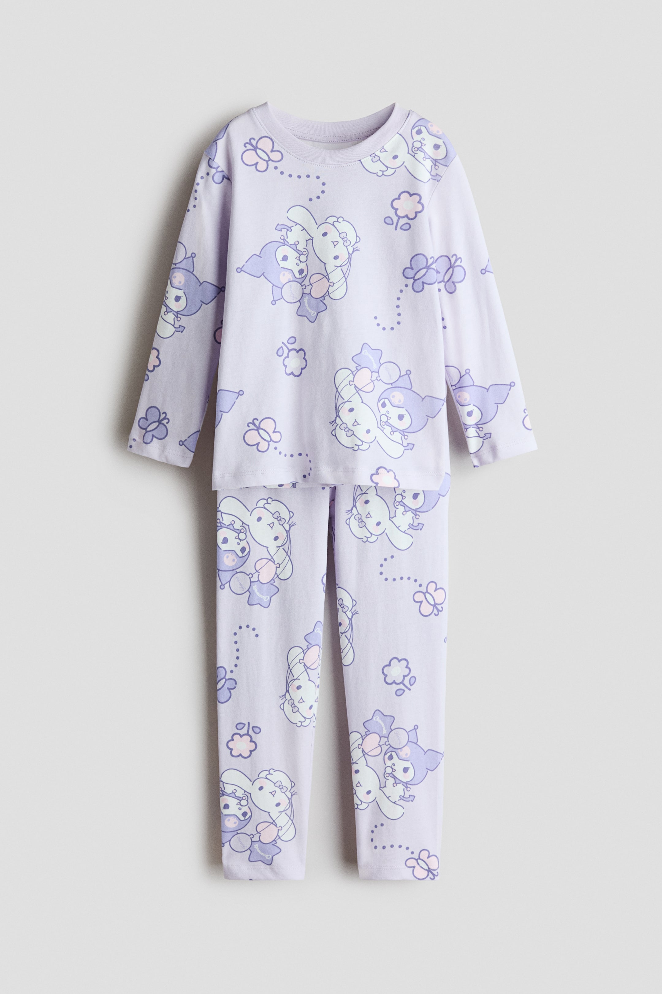 View larger image: A light purple pyjama set is laid flat, consisting of a long-sleeved crew neck top and long pants. It features a repeating pattern of light blue and purple cartoon characters, butterflies, and dotted lines.