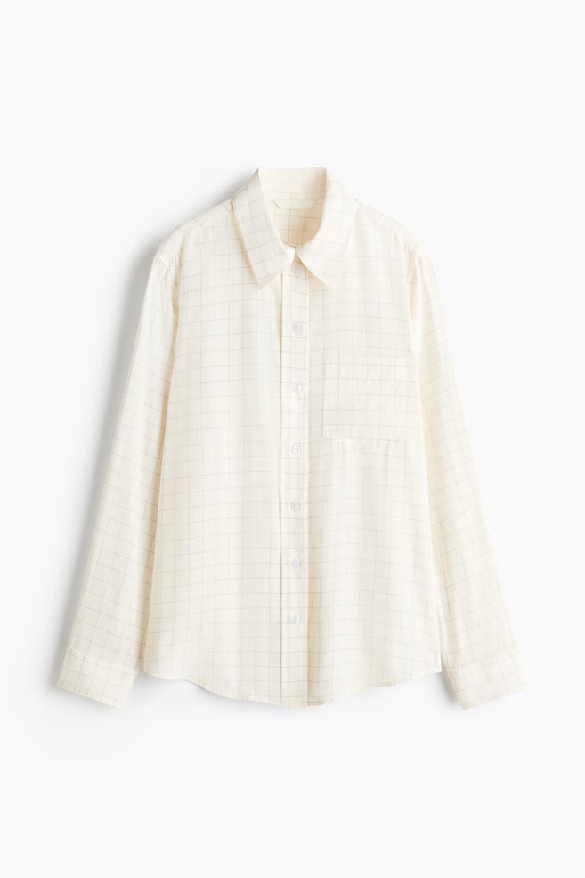 A long-sleeved button-up shirt is hanging in a front-facing view, featuring an off-white fabric with a thin grid pattern. The shirt is displaying a point collar, a full-length button placket, a single patch pocket on the left chest, and buttoned cuffs. - 1
