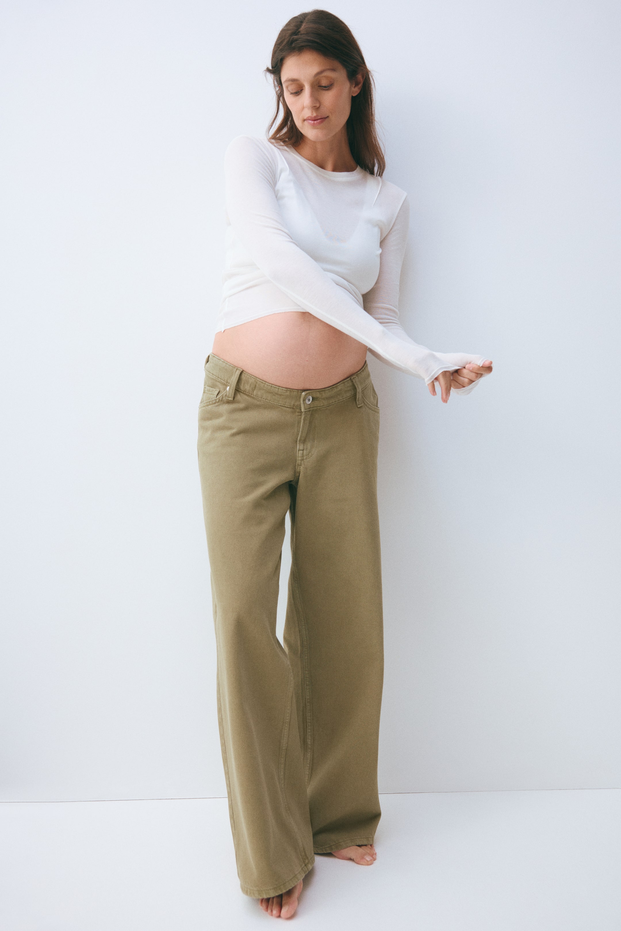 View larger image: Khaki green wide-leg pants feature a low-rise waistband with a visible button closure and front pockets. These pants showcase a relaxed, wide fit through the leg, facing forward.