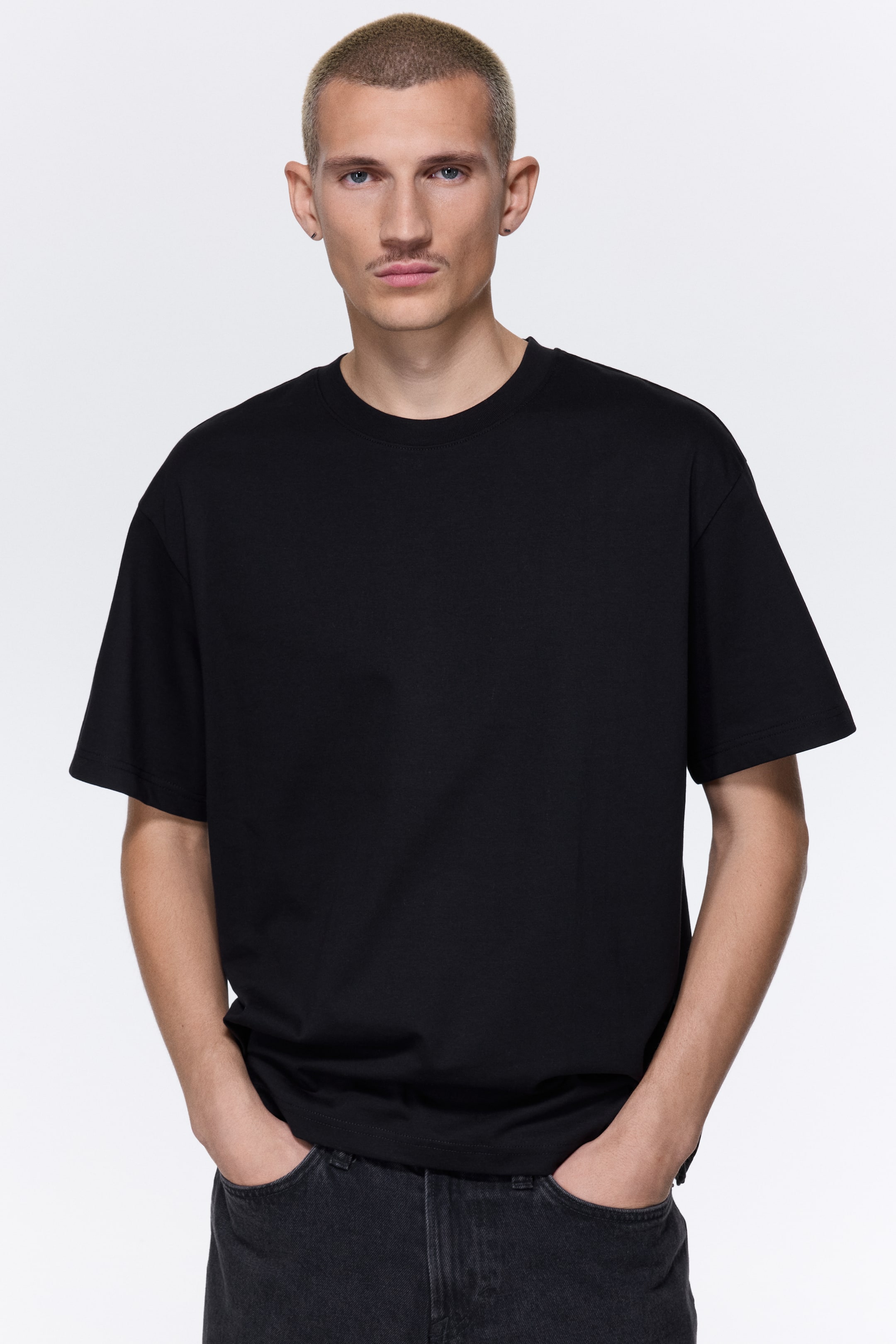 View larger image: A black t-shirt is featuring a crew neck and short sleeves, presenting an oversized fit. Its straight hem is falling just below the waistline, over dark jeans.