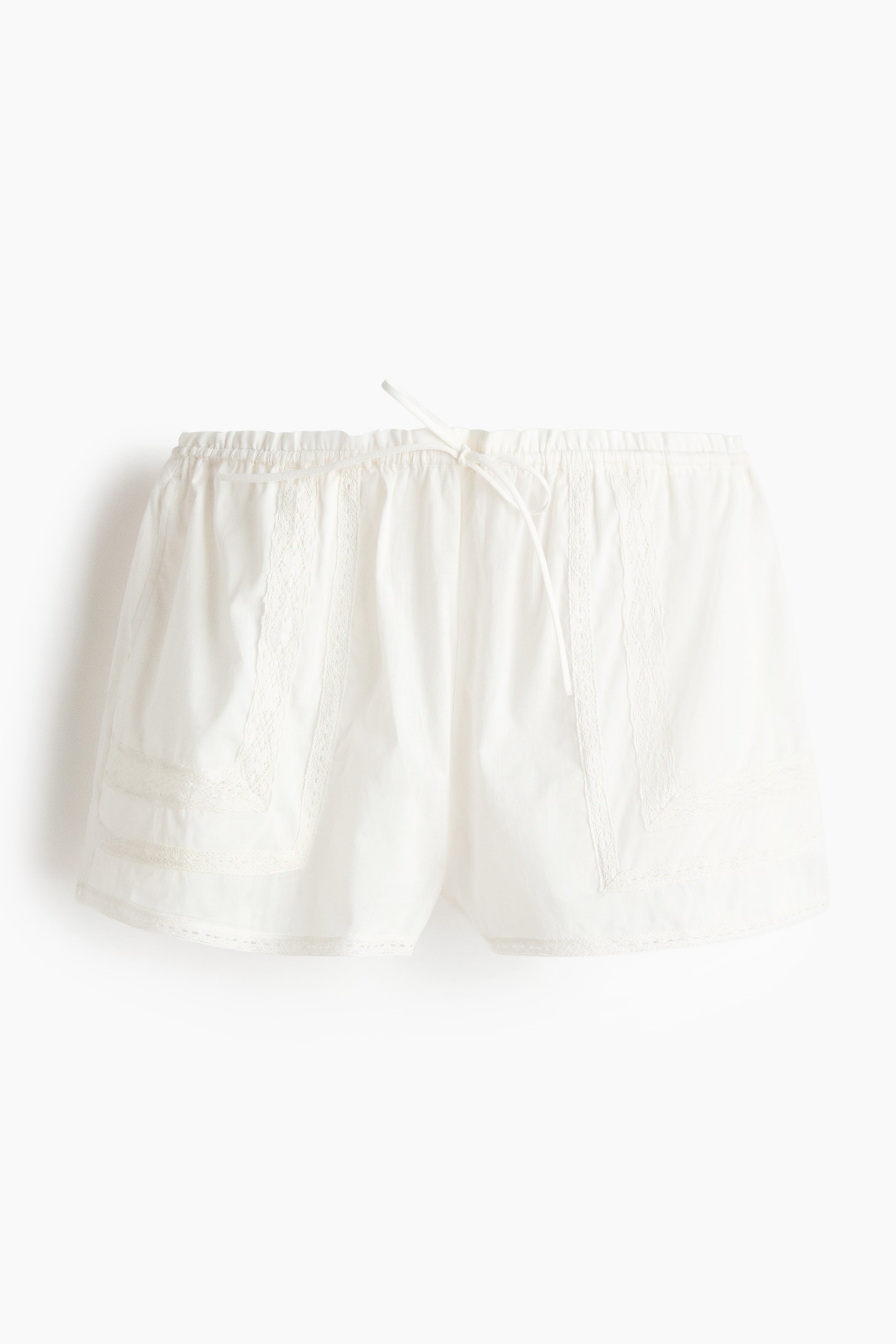 View larger image: White beach shorts are shown from the front, highlighting a breezy cotton weave and delicate lace insets. They feature a frill-trimmed waist with covered elastic and a drawstring, along with patch side pockets and lace-trimmed hems.