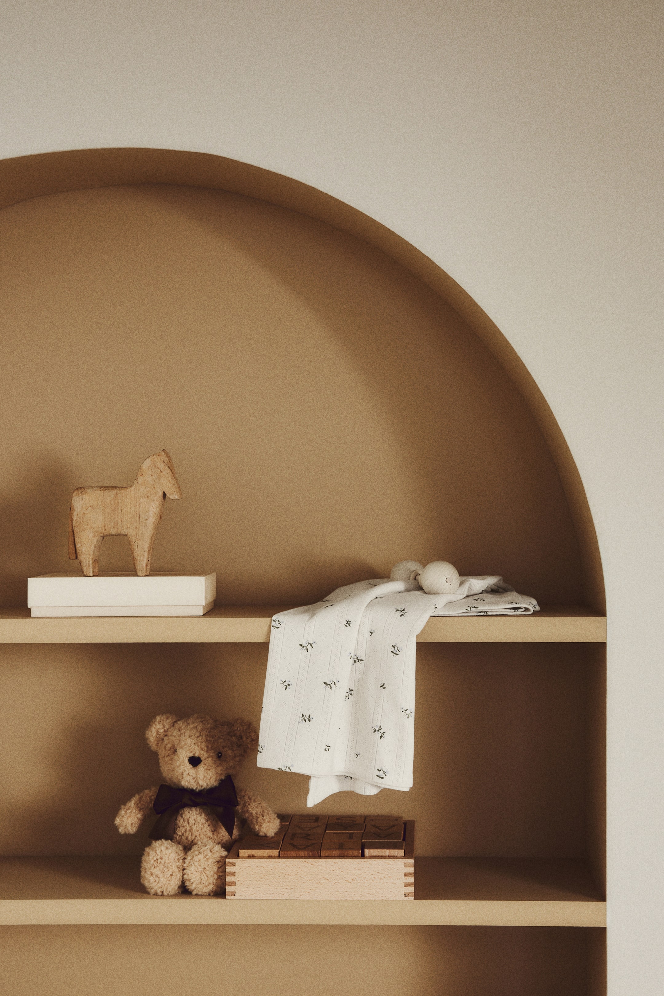 Visualizza l'immagine ingrandita: Una morbida coperta per neonati in cotone a maglia pointelle è posata su uno scaffale, mostrando una stampa floreale classica con piccoli motivi scuri sulla sua superficie chiara.
