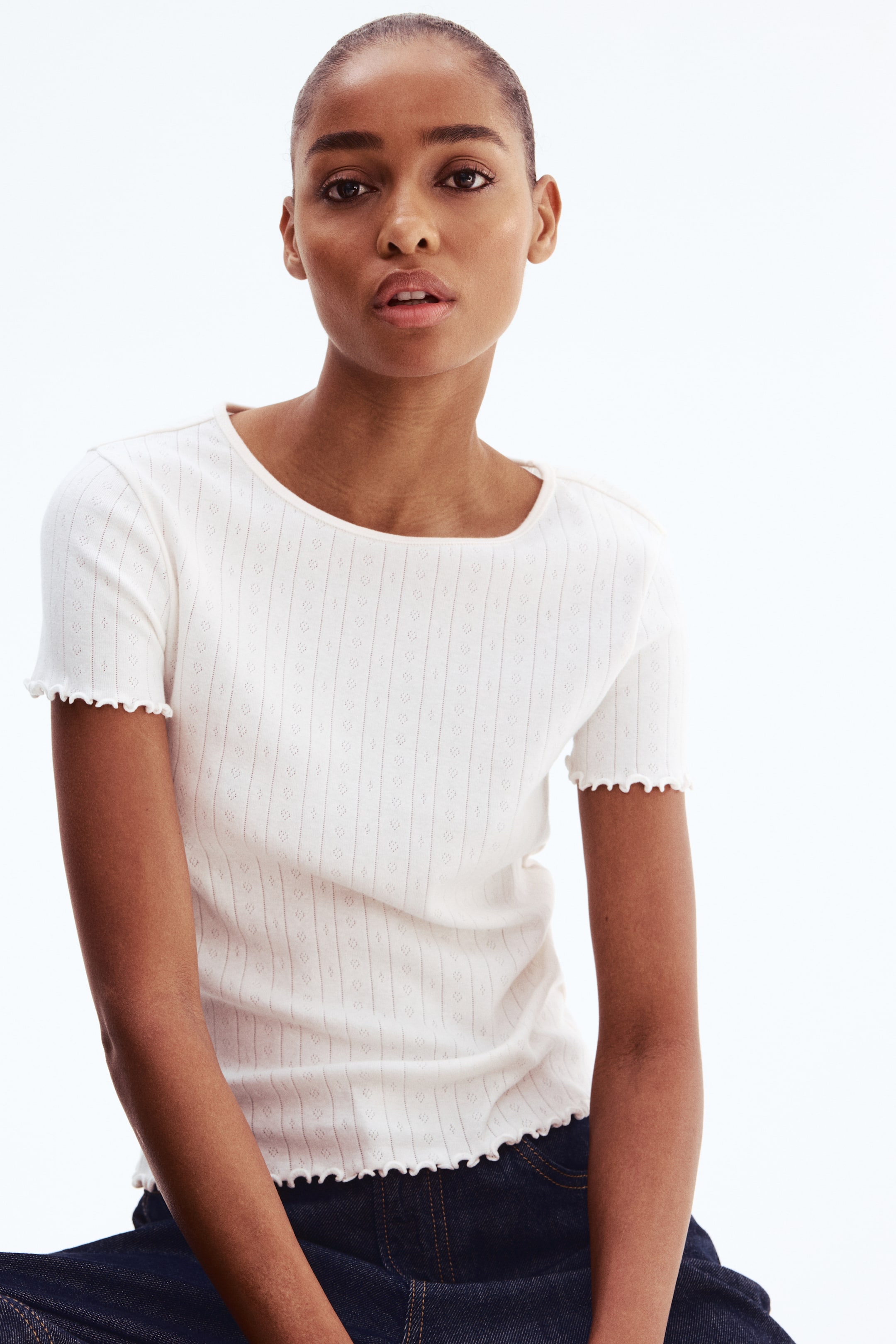 View larger image: A white short-sleeved top features a wide, rounded neckline and is detailed with vertical rows of small eyelet patterns. The short sleeves and bottom hem are finished with scalloped edges.