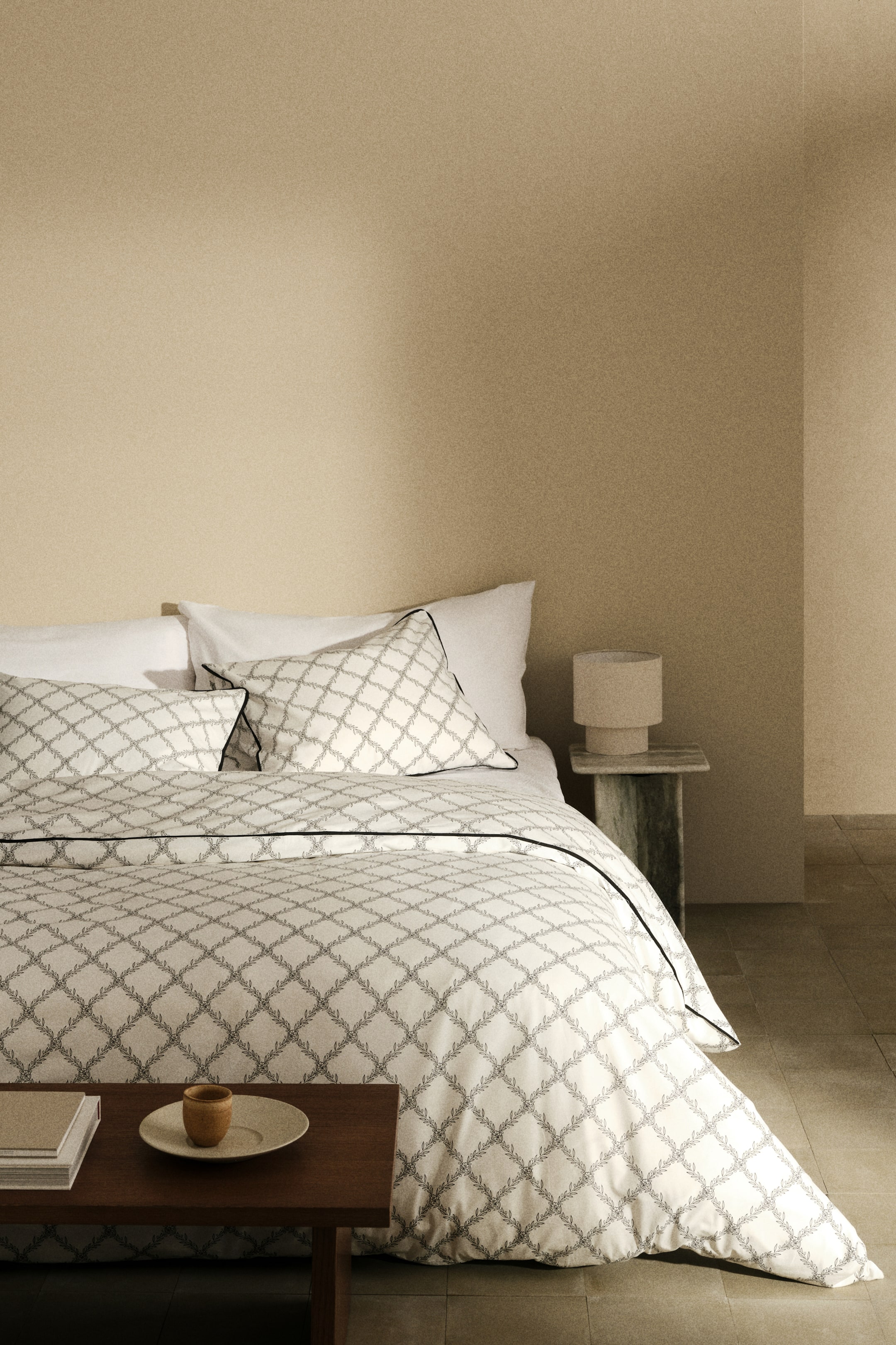 View larger image: A white duvet cover and two matching pillow shams feature a diamond lattice pattern of leaf motifs. Black piping outlines the edges of the duvet cover and pillow shams.