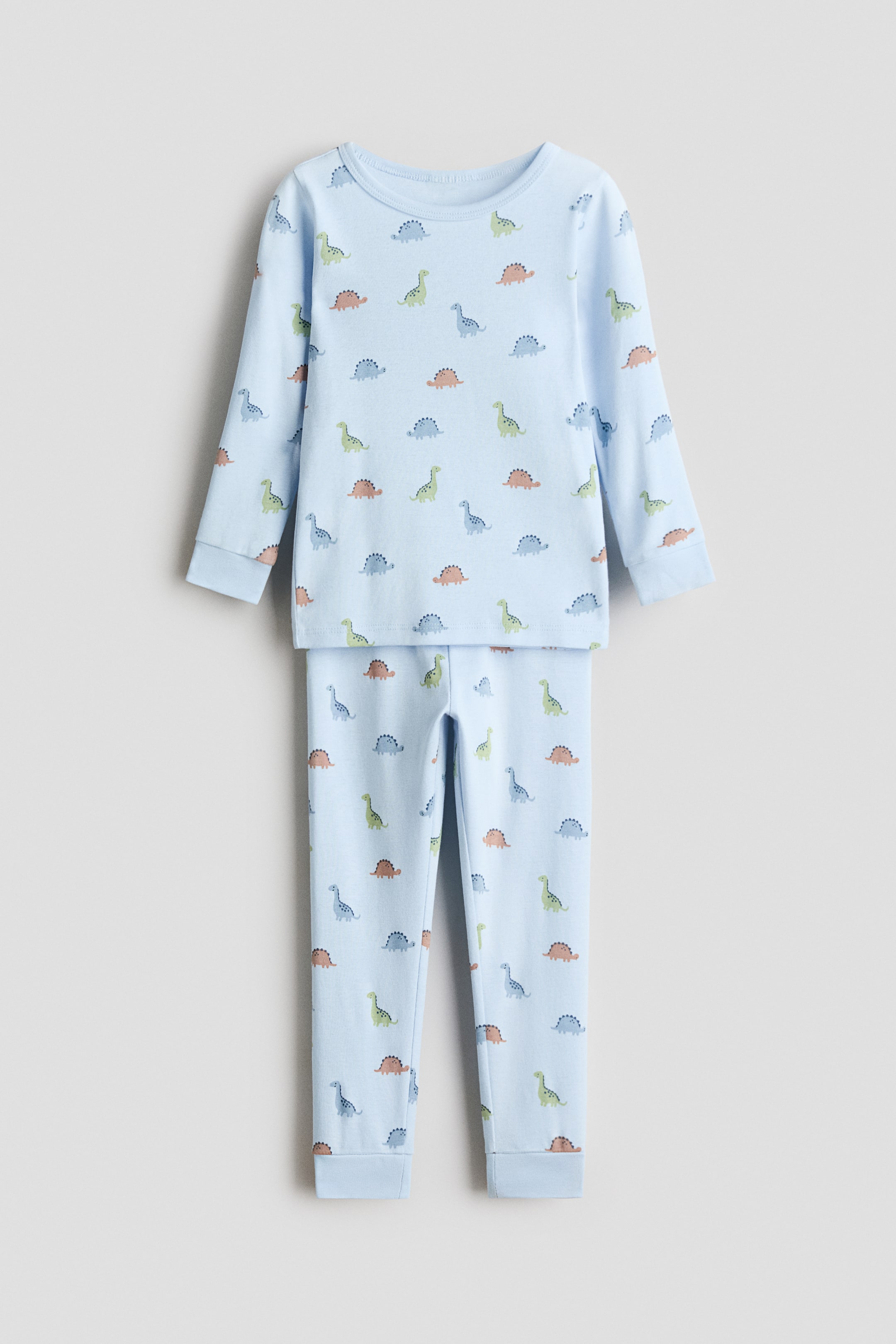 View larger image: Snug Fit printed cotton pajamas present FRONT as a light blue two-piece set. The long-sleeved top features a crewneck and an all-over pattern of small multicolored dinosaurs, while the matching long pants have cuffed ankles, both designed for a snug fit.