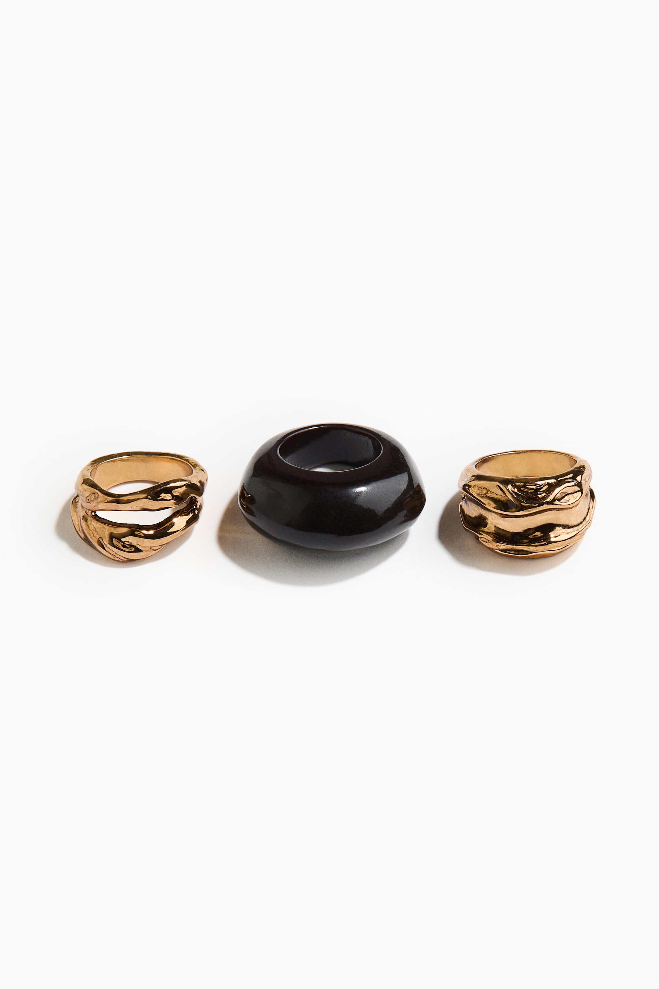 View larger image: Three rings are arranged side-by-side. Two gold-toned rings are featuring a wide, textured, and undulating design. The third ring is presenting a thick, smooth, dark brown band with a glossy finish.