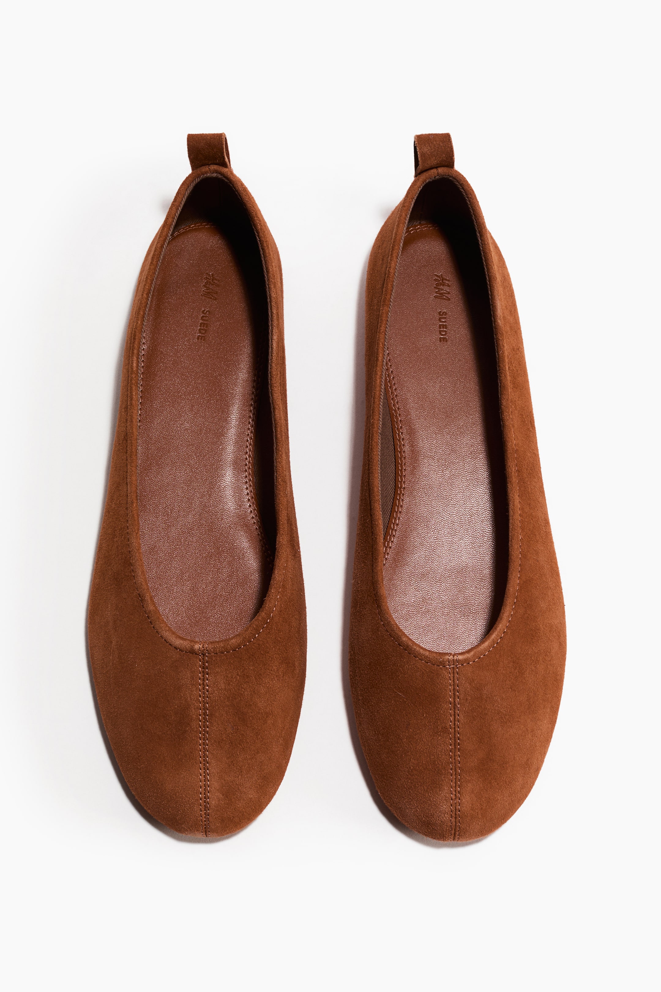 View larger image: A pair of brown suede ballet flats is presenting from above, showing rounded toes and small pull tabs at the heels. A vertical seam is running from the toe of each flat, and a brown insole is displaying "H&M SUEDE" lettering.