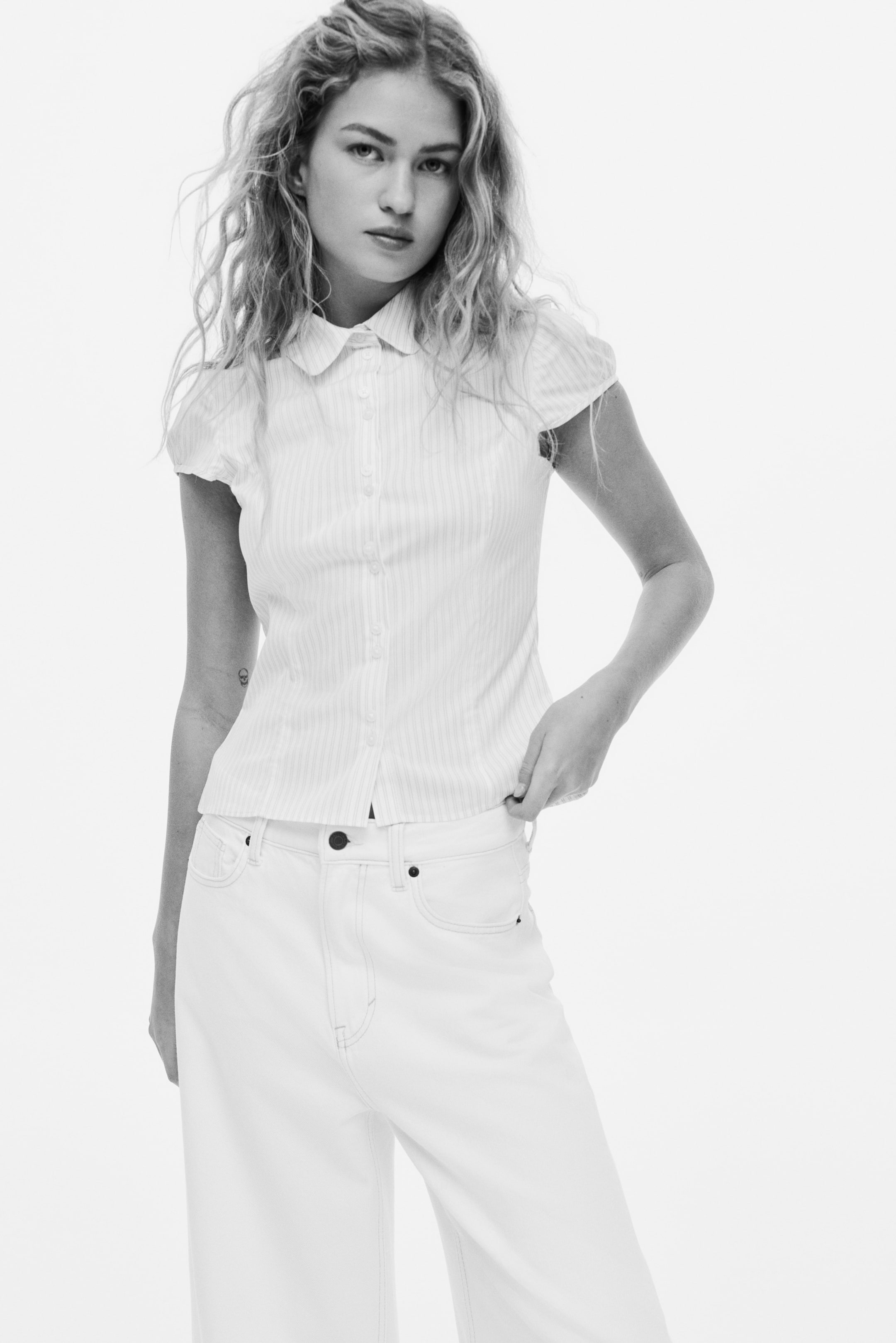 View larger image: A white short-sleeve button-up shirt with a Peter Pan collar and subtle vertical stripes is worn partially untucked with white high-waisted wide-leg jeans featuring contrast stitching and front pockets.
