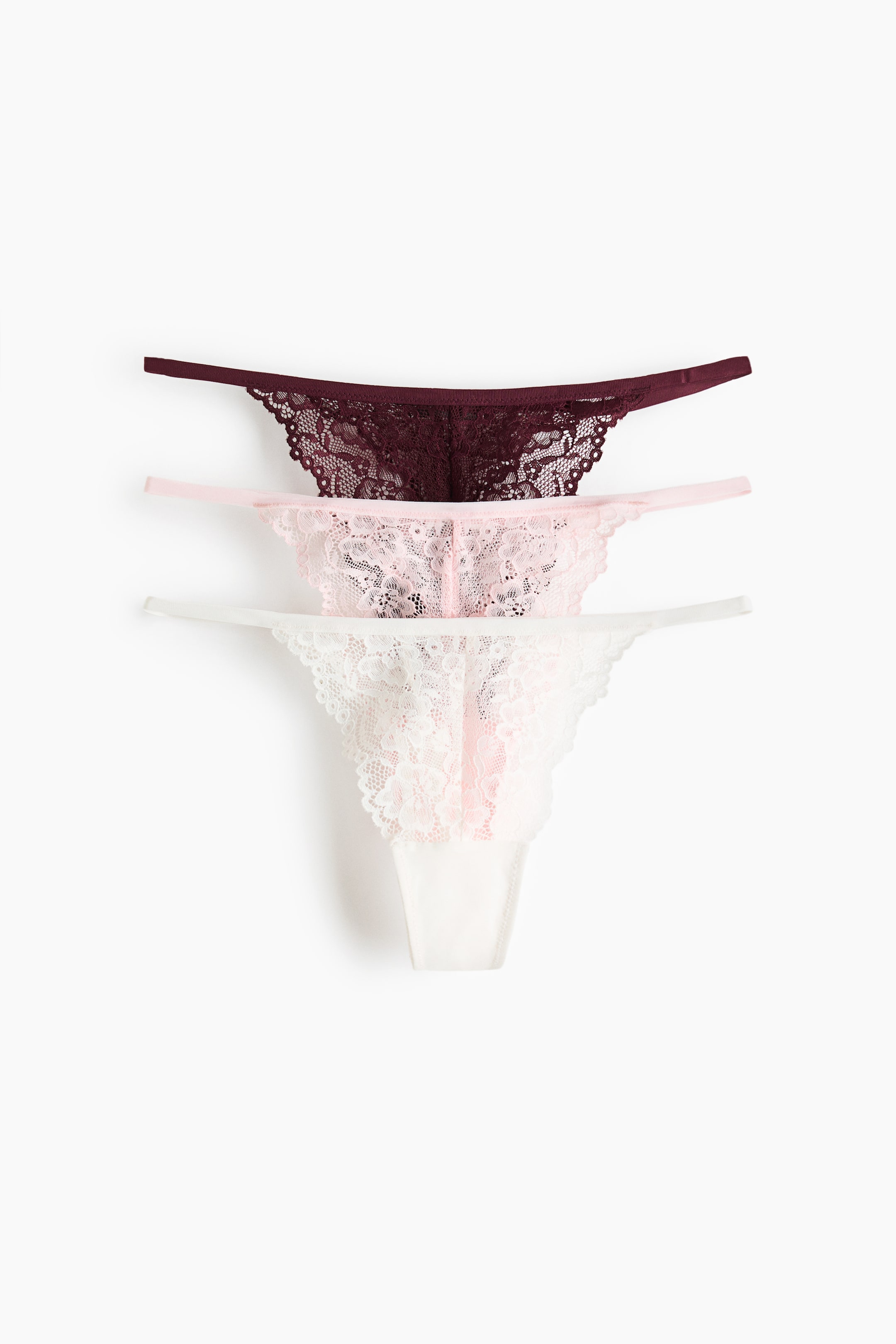 View larger image: Three thong briefs are displayed front-facing, each showcasing a lace pattern, a low-rise waist, slender sides, and a lined gusset. They come in shades of dark red, light pink, and white.