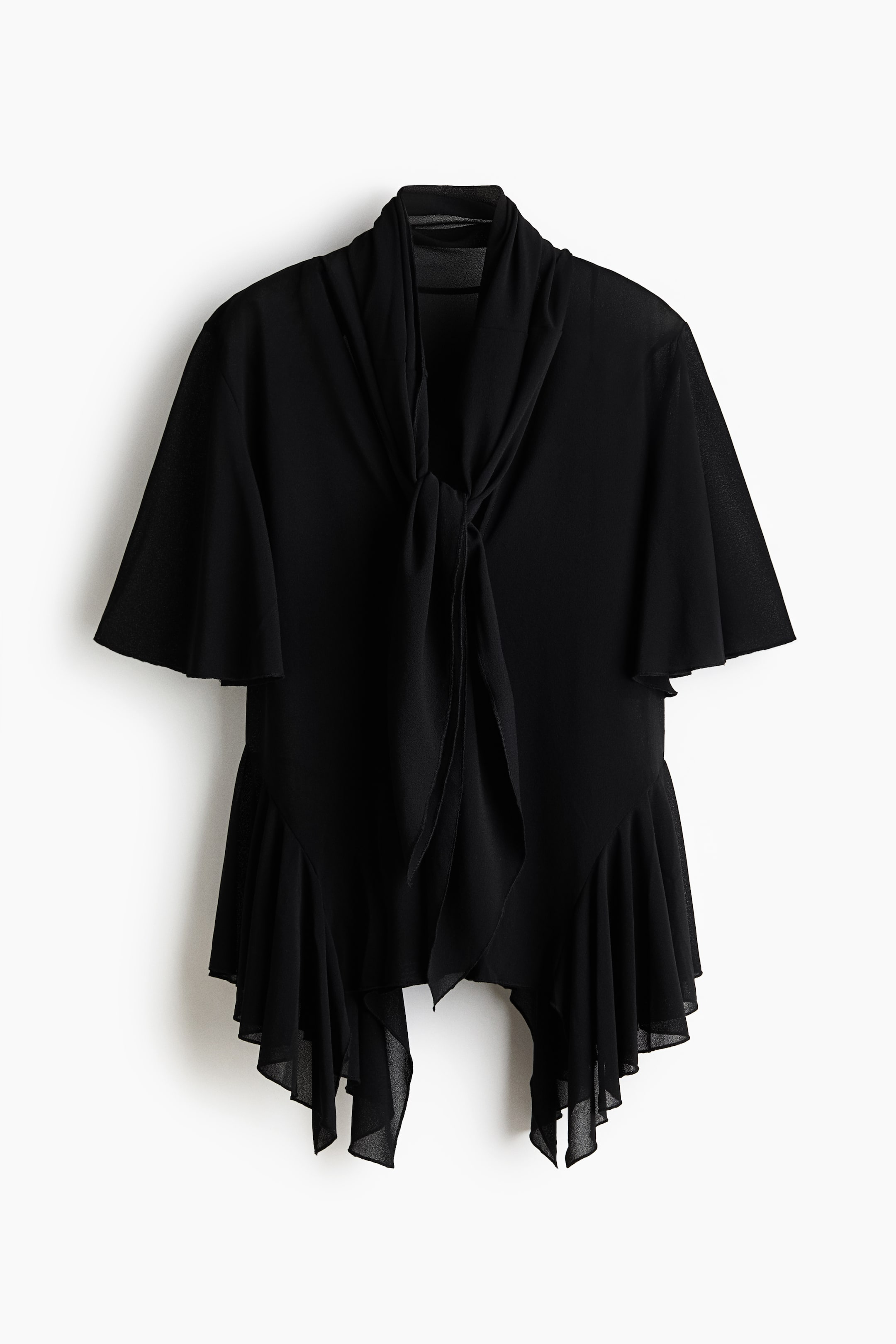 Visa större bild: En svart blus med framsidan framåt har en draperad knytkrage, korta vida fladdriga ärmar och en asymmetrisk volangkant.
