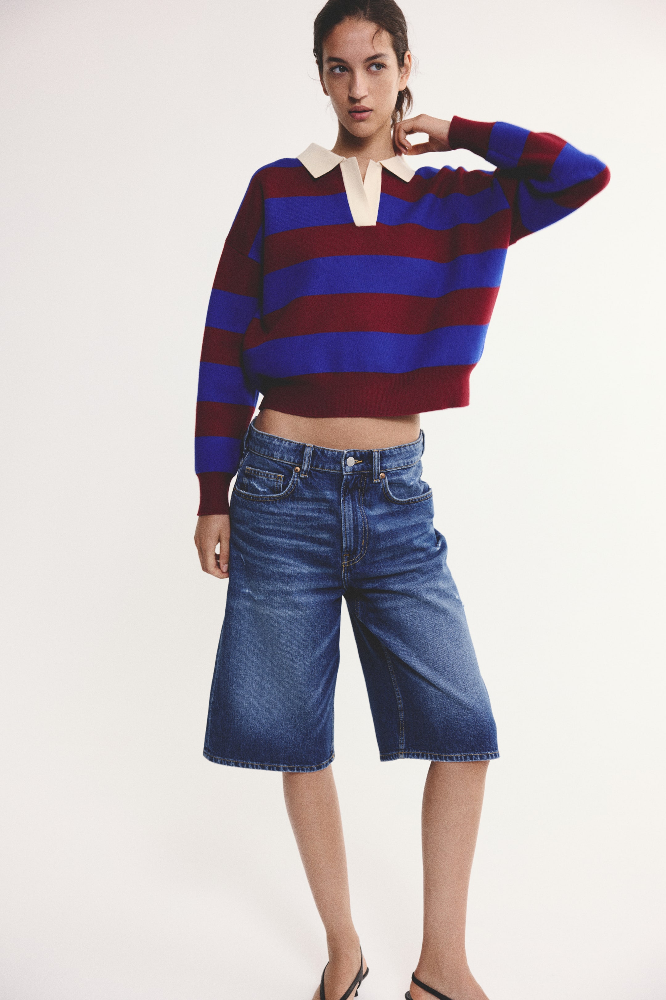 Visualizza l'immagine ingrandita: Una polo in maglia corta e oversize con righe orizzontali blu e bordeaux indossata dalla modella. La maglia presenta un colletto aperto color crema a contrasto, spalle scese e polsini a costine, ed è abbinata a shorts in denim blu.