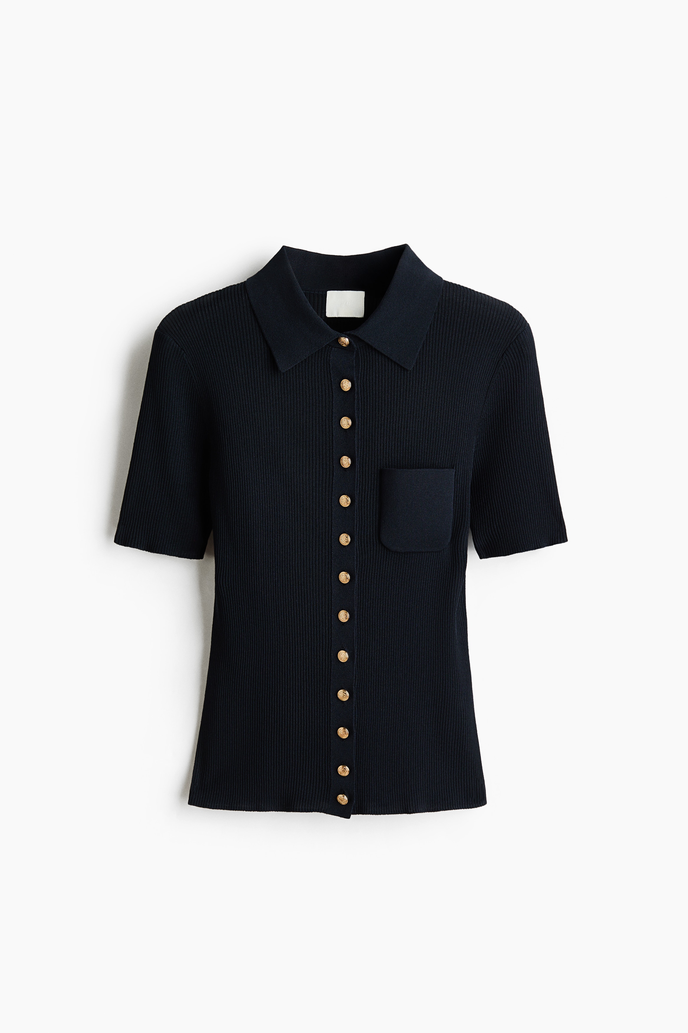 A black, short-sleeved cardigan in a fine rib-knit is being worn by the model, featuring a collar, a patch pocket on the chest, and embossed gold-tone buttons down the front. The cardigan is styled with white trousers, with the bottom buttons left unfastened at the waist.