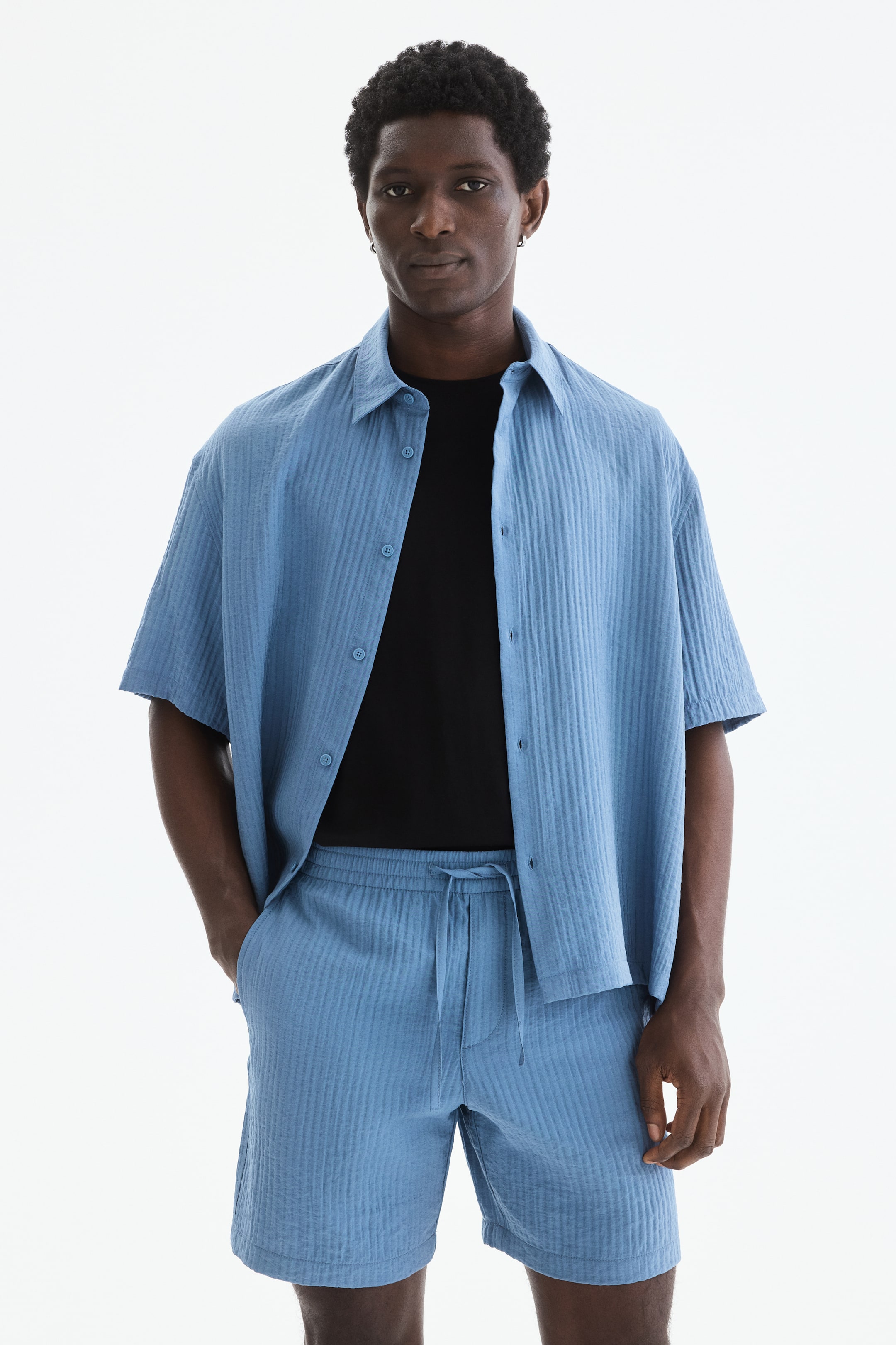 View larger image: Presenting a light blue short-sleeved shirt paired with matching shorts, both crafted from a vertically textured fabric. The shirt, featuring a pointed collar and front buttons, is styled open over a black t-shirt, while the shorts come with an elasticated drawstring waist for a comfortable fit.