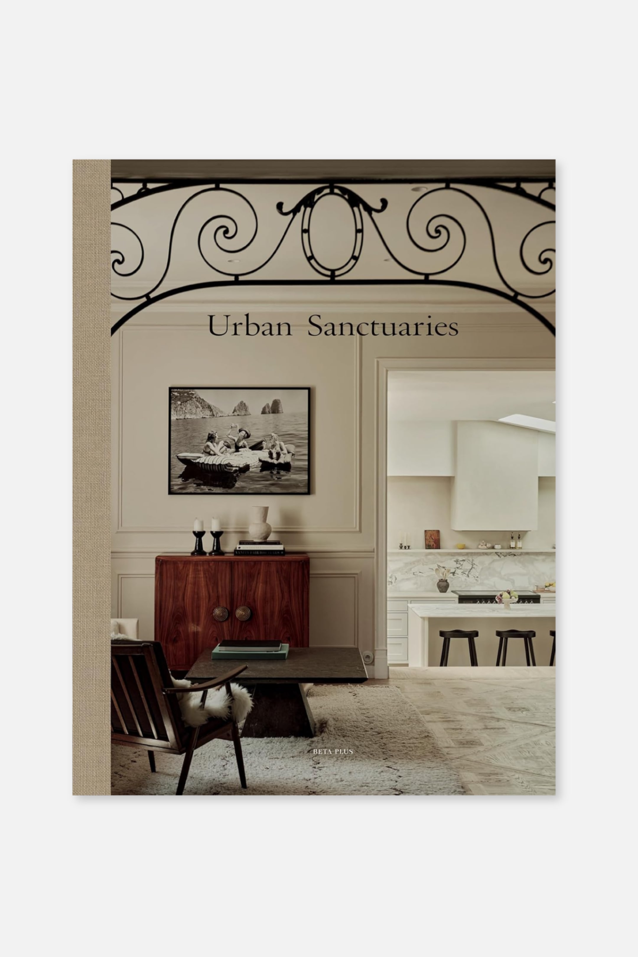 Größeres Bild ansehen: Ein Buch steht aufrecht und nach vorne gerichtet, zeigt ein Cover mit einer Innenszene, die schwarze Schmiedeeisenbogen-Details aufweist, den Titel "Urban Sanctuaries", ein Schwarz-Weiß-Foto, eine moderne Küche, die durch eine Türöffnung sichtbar ist, und "BETA PLUS" in kleiner Schrift. Der linke Buchrücken besteht aus einem strukturierten, hellbraunen Material.