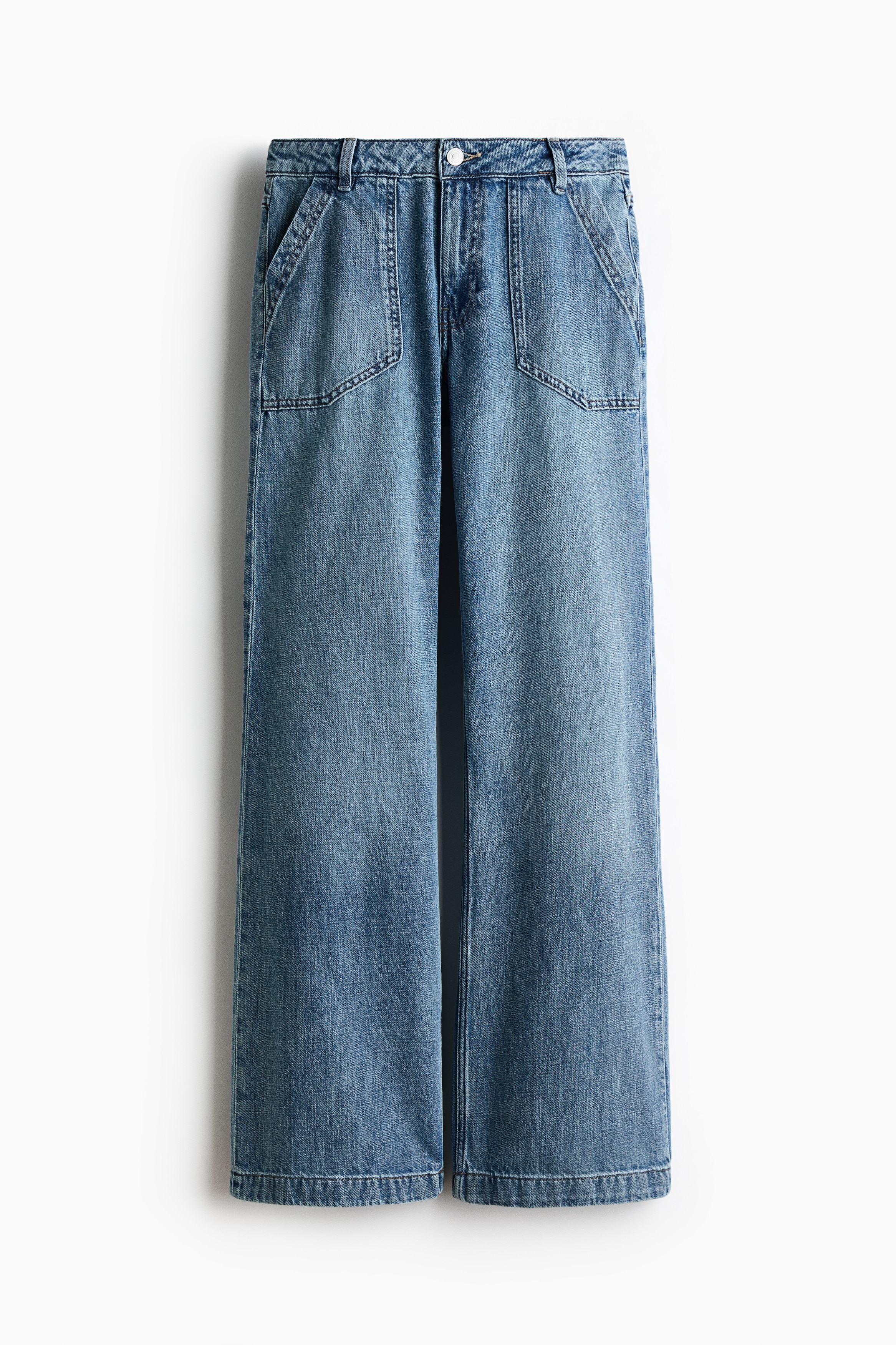 Blue wide-leg denim jeans featuring a relaxed fit and prominent diagonal front pockets are being worn by the model. The jeans are paired with a layered, grey-striped T-shirt and beige trainers.