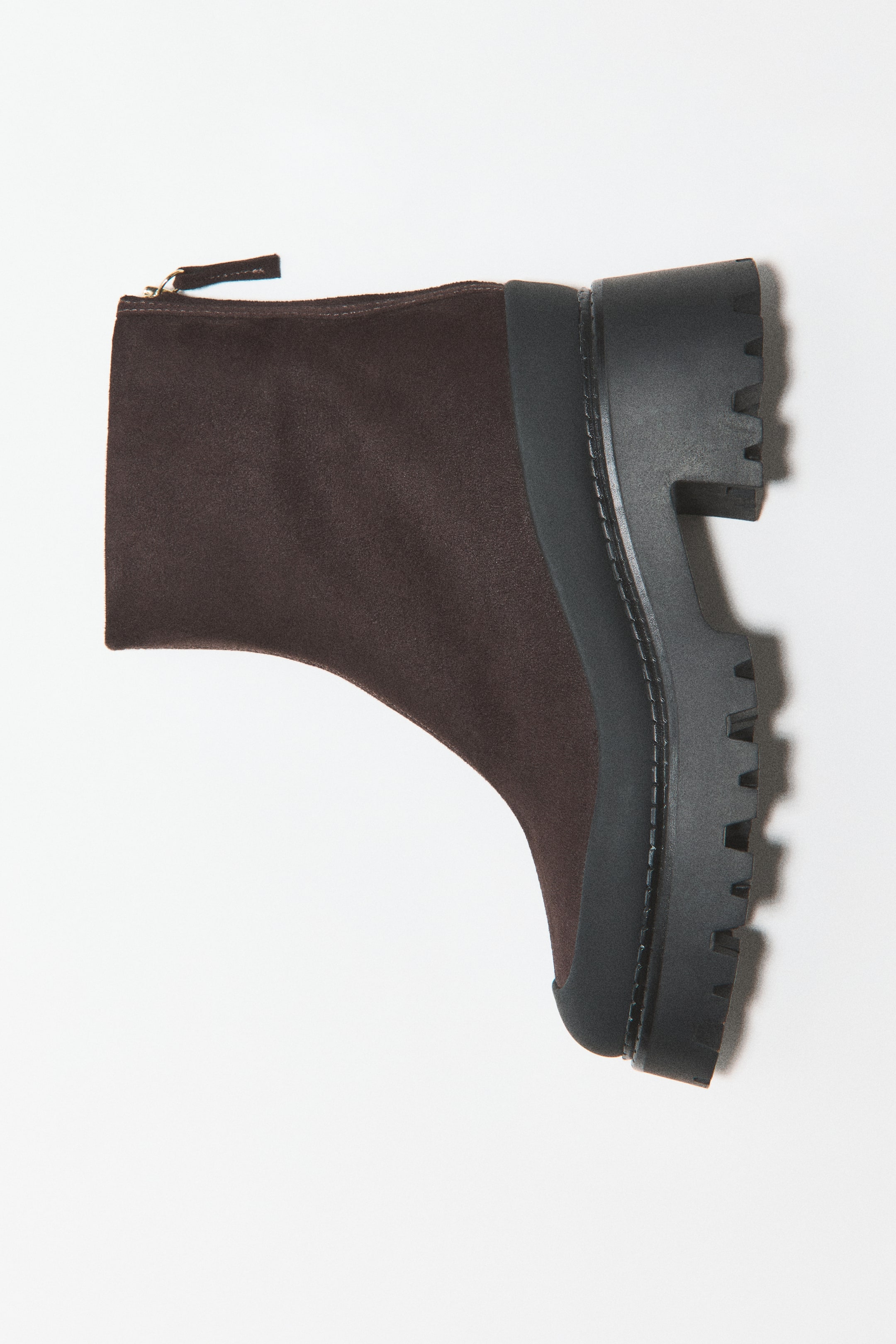 View larger image: A dark brown ankle boot is shown in side profile, featuring a soft fabric upper and a black rubber mudguard wrapping around the base. The boot features a chunky, lugged block sole with patterned tread and a concealed zip at the back of the ankle.