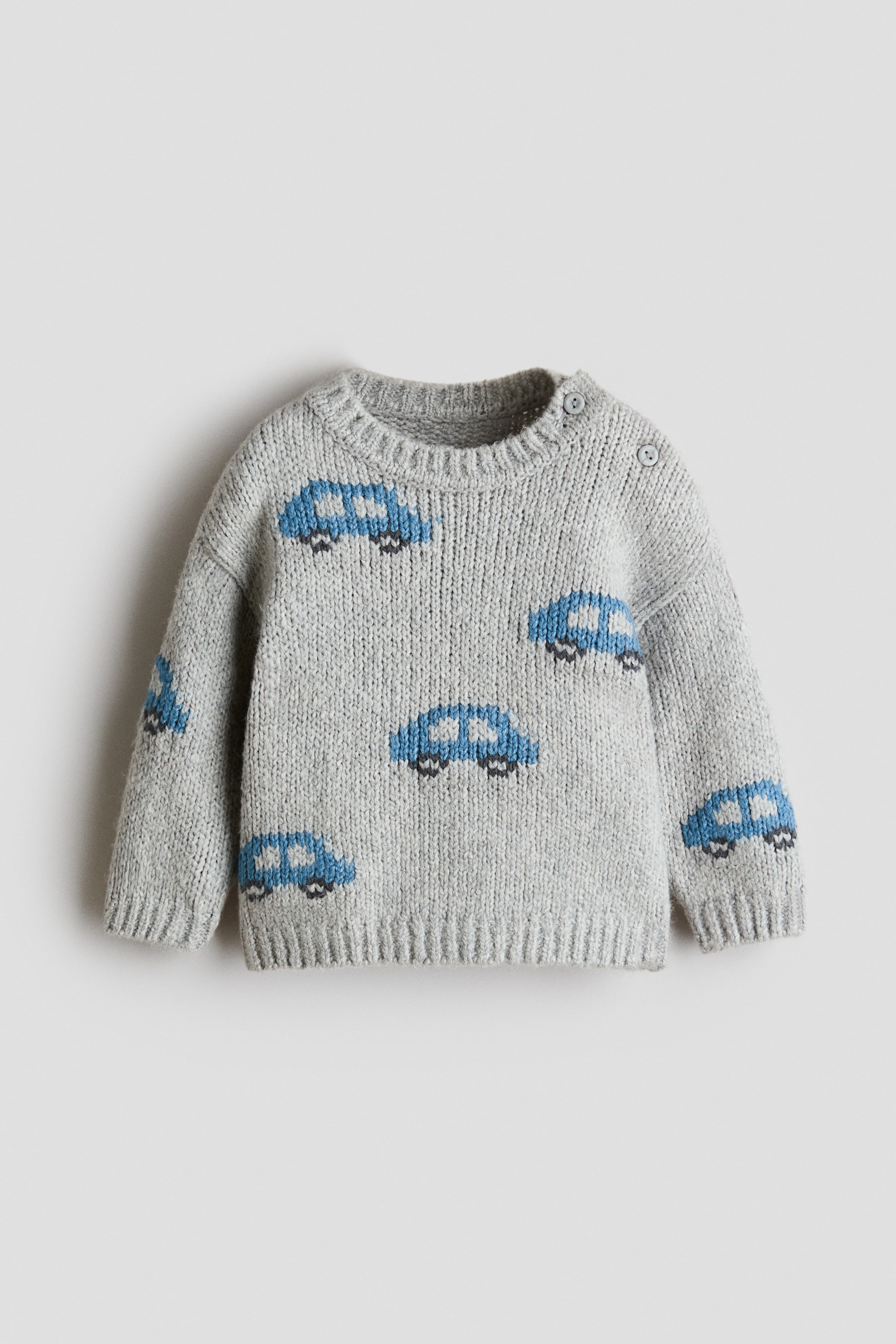 View larger image: A light grey knitted baby jumper is showcasing blue car motifs across the front and sleeves, facing forward. It features a crew neck with two grey buttons on the left shoulder, ribbed cuffs, and a ribbed hem.