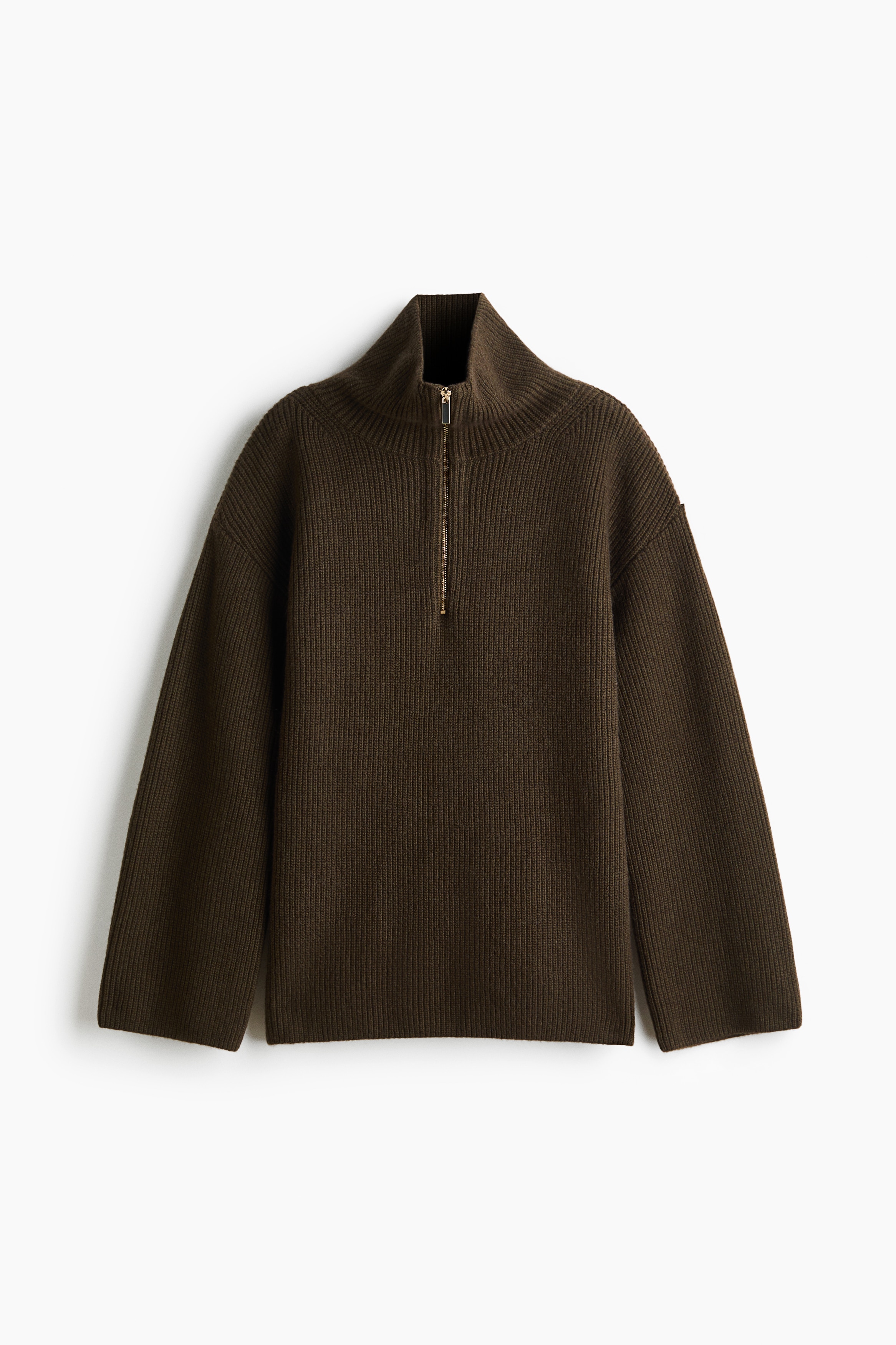 Ein dunkelbrauner, englisch gerippter Strickpullover wird vom Model getragen und zeichnet sich durch einen hohen Kragen mit goldfarbenem Half-Zip, überschnittene Schultern sowie weite Ãrmel mit umgeschlagenen Bündchen aus. Der gerade Saum des Pullovers hat Seitenschlitze, durch die das Model seine Hände in die Taschen der blauen Jeans steckt.