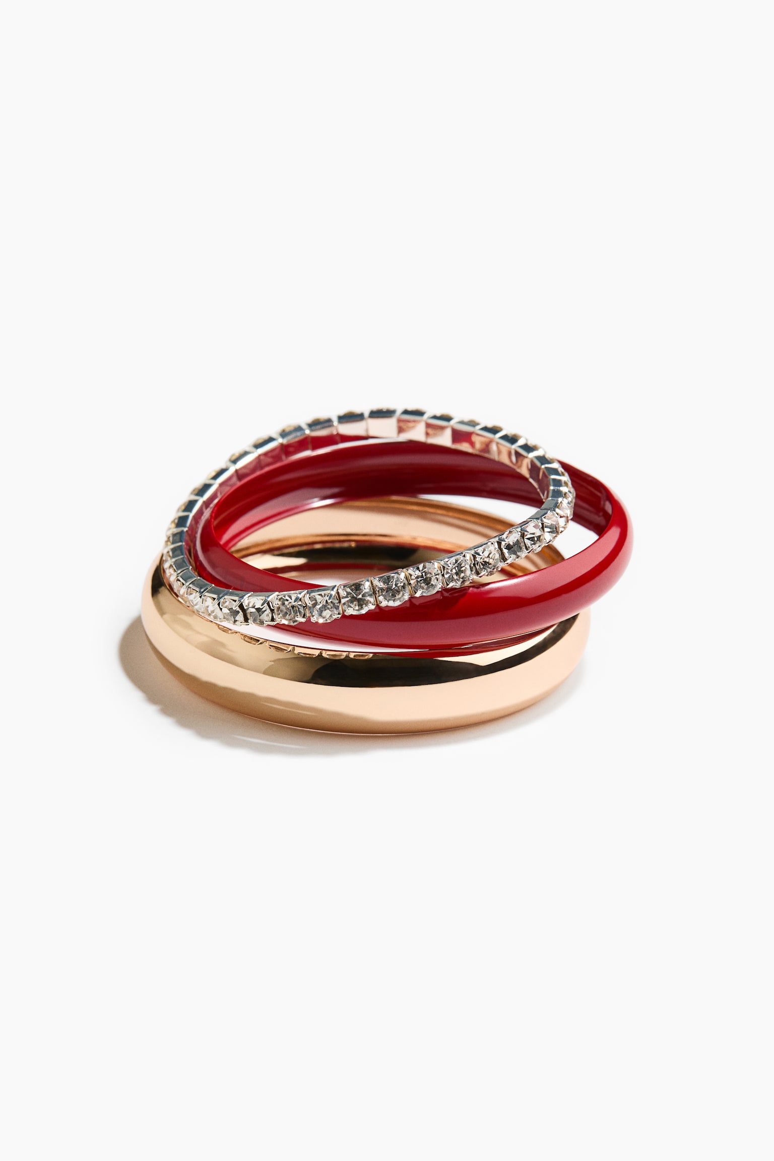 Un juego de cuatro brazaletes rÃ­gidos estÃ¡ apilado y encajado entre sÃ­ visto de frente, con una banda ancha de tono dorado pulido en la base. Encima descansan una banda mÃ¡s delgada de tono dorado, una banda de esmalte rojo brillante y una banda delgada de tono plateado adornada con una hilera de rhinestones transparentes de corte cuadrado.