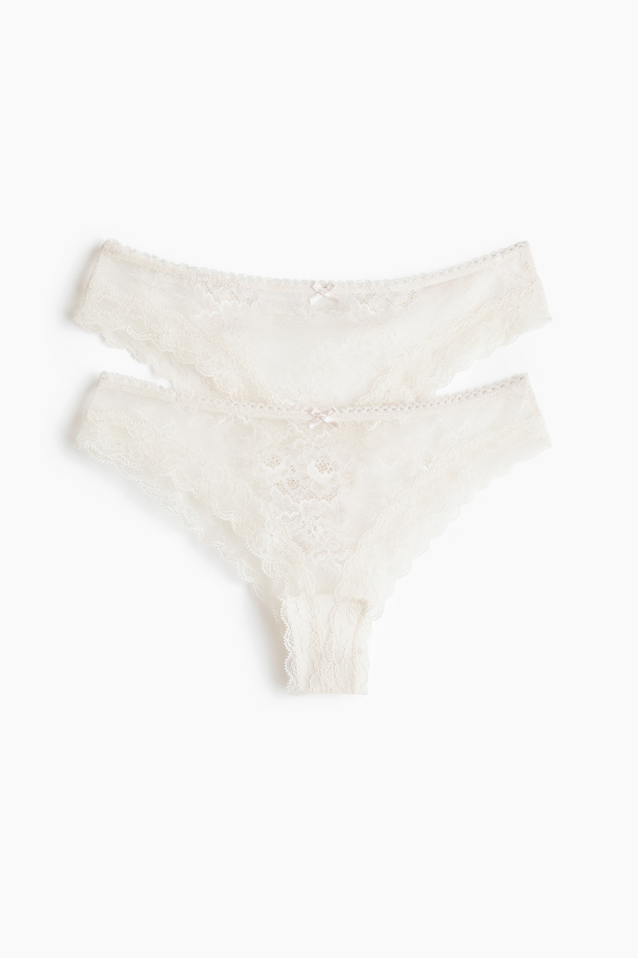 Agrandir l'image: Deux strings en dentelle blanc cassé sont posés à plat, l'un chevauchant légèrement l'autre, chacun arborant un délicat motif de dentelle florale avec des bords festonnés et un petit nœud à l'avant de la taille.