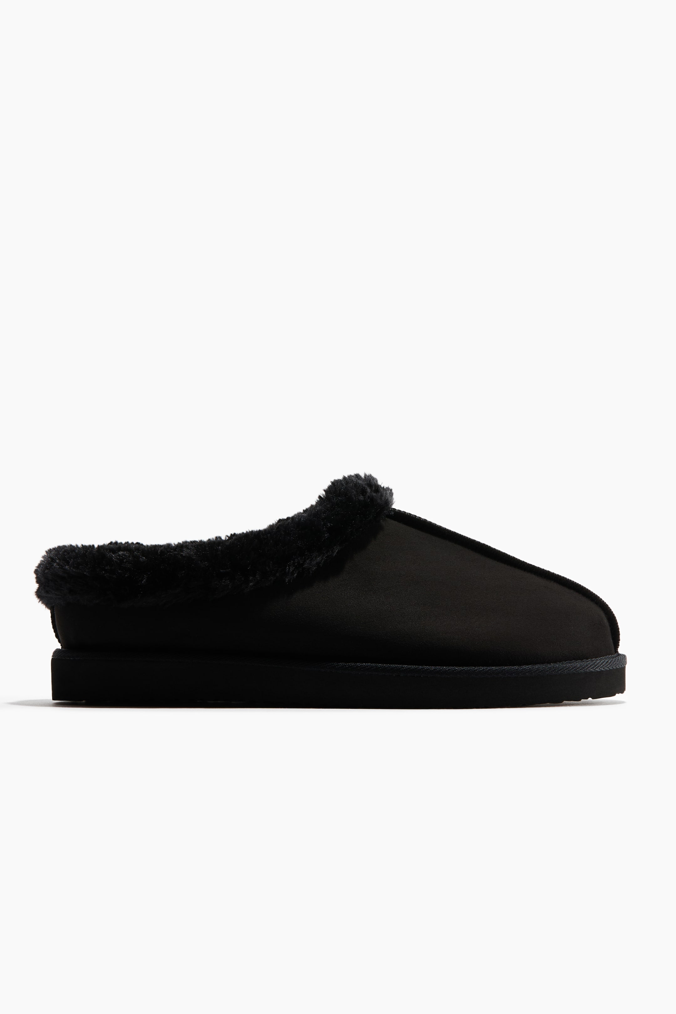 Agrandir l'image: Une pantoufle noire en daim à enfiler est présentée en vue de profil, avec un col et une doublure en shearling noir moelleux. La pantoufle présente une couture centrale courant le long de l’avant de la tige et repose sur une semelle noire plate et épaisse.