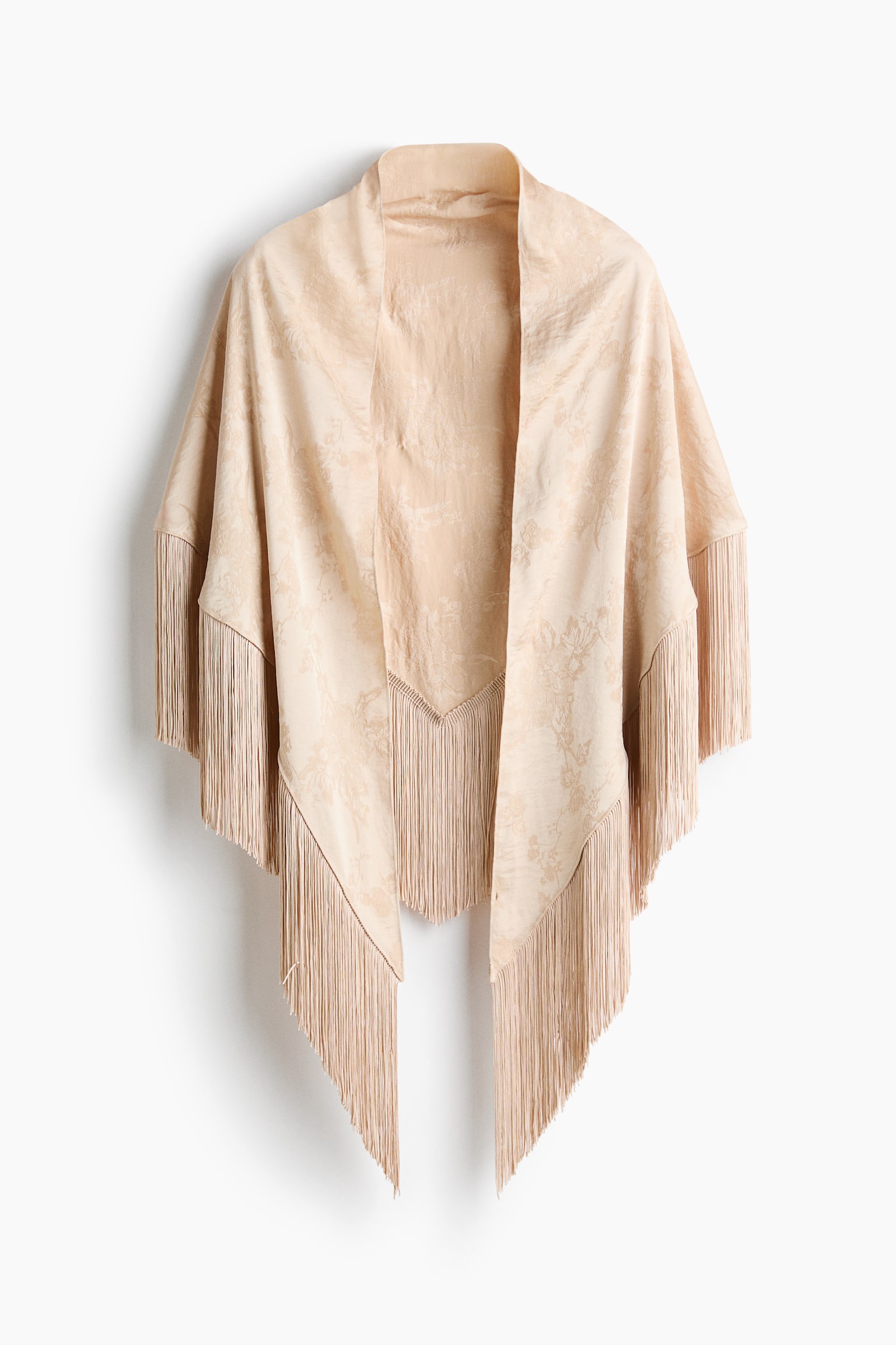 A beige open-front wrap is hanging front-facing, showcasing a subtle tonal floral jacquard pattern. The garment features long matching fringe trim draping along the wide sleeves and the pointed asymmetric hemline. - 1