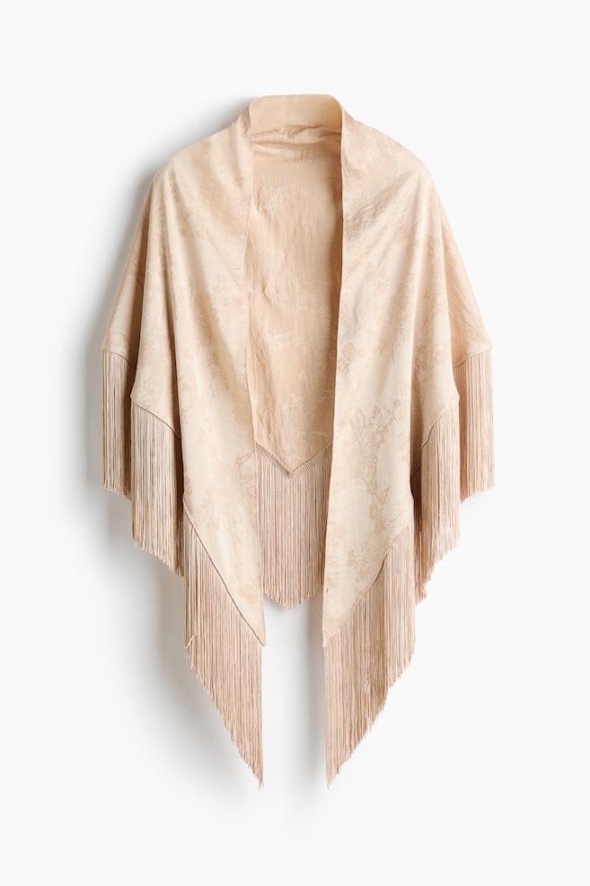 En beige Ã¥pen front-wrap henger vendt mot front, og viser et subtilt, tonalt blomsterjacquardmÃ¸nster. Plagget har lange, matchende frynsekanter som faller langs de vide ermene og den spisse, asymmetriske nederkanten. - 1